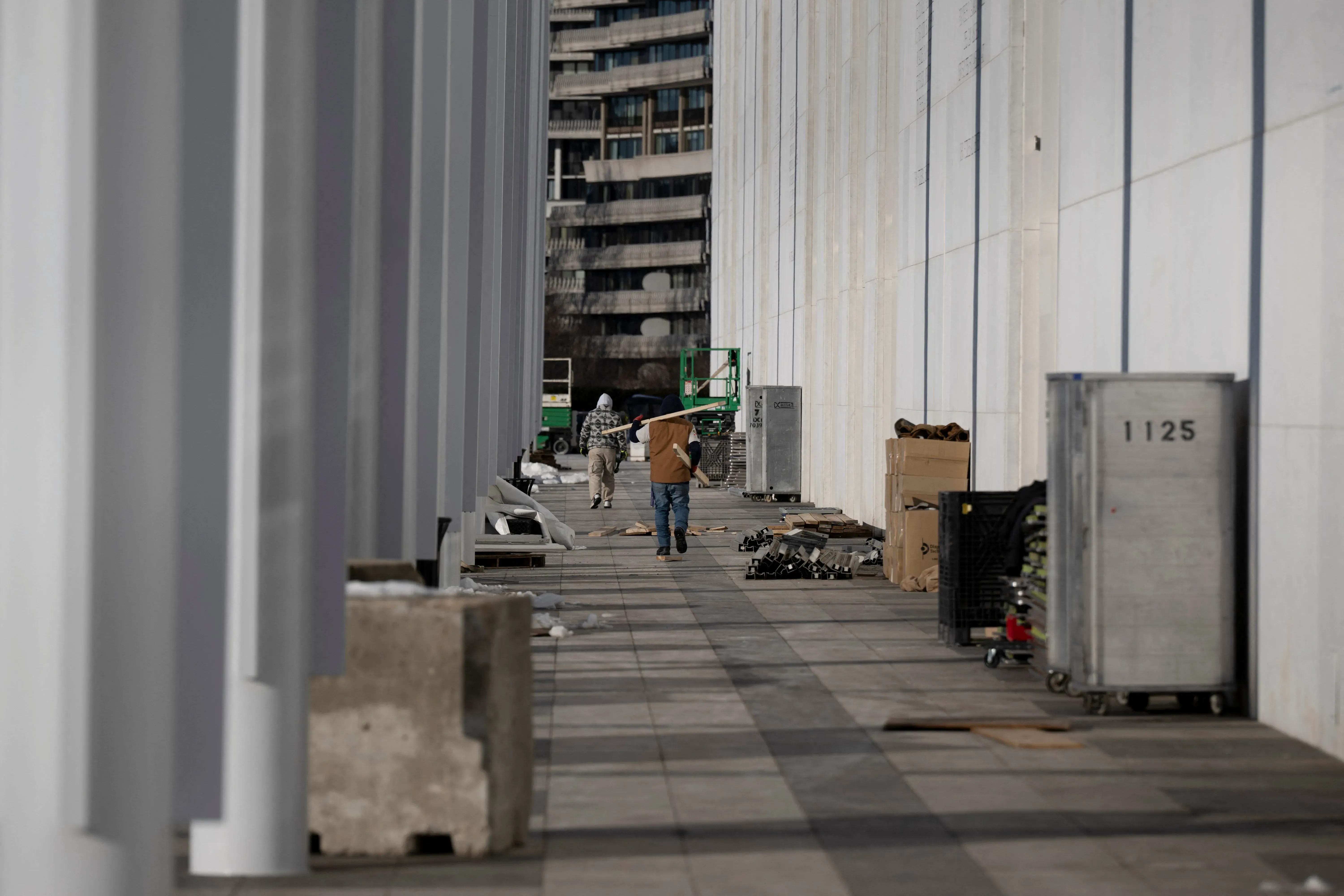 عمال يقومون بأعمال تجديد في مركز كينيدي، مع وجود صناديق وأدوات على الأرض، بينما تظهر أعمدة المبنى البيضاء في الخلفية.