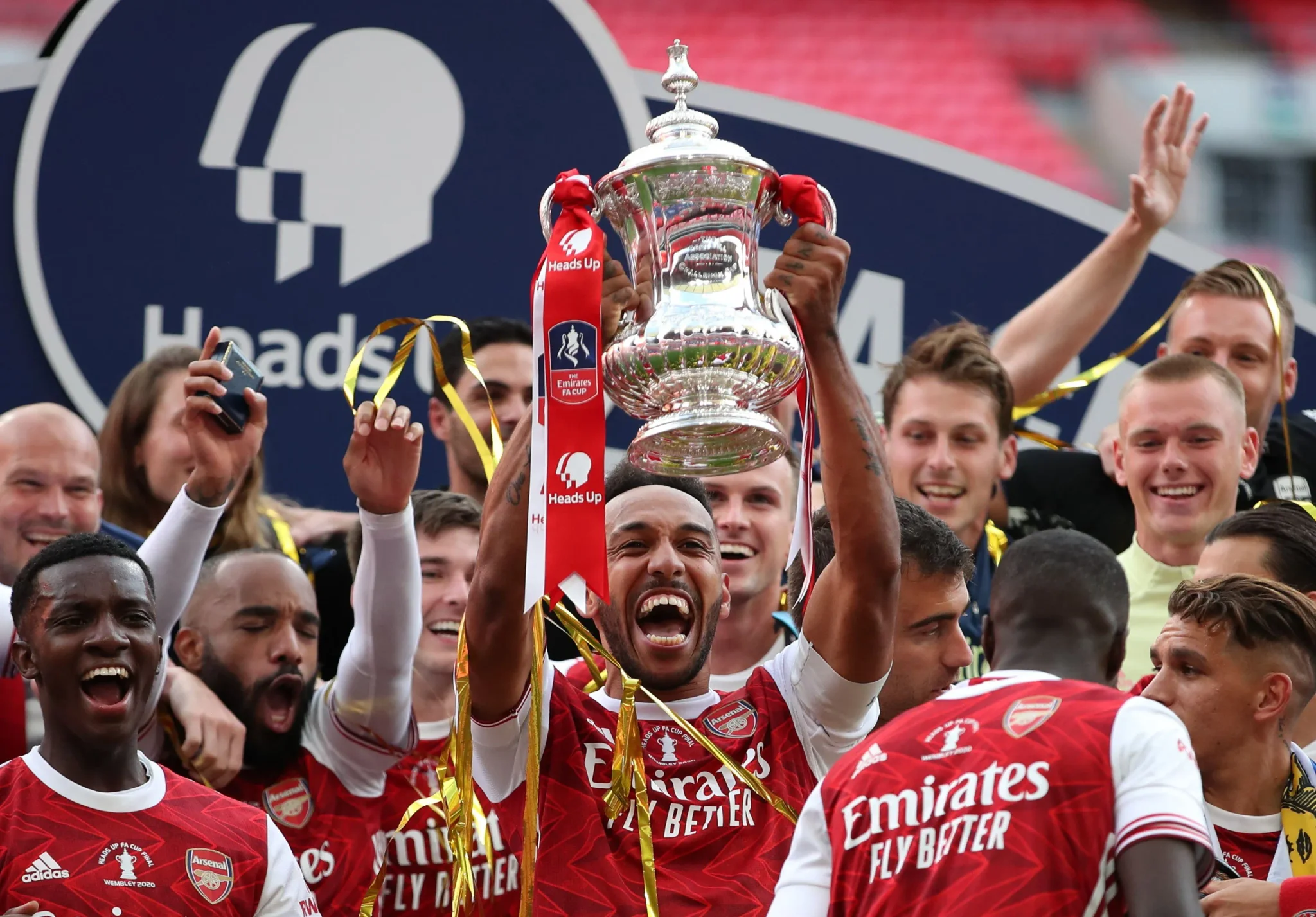 فريق Arsenal يحتفل بفوزهم بكأس FA، حيث يحمل اللاعبون الكأس وسط أجواء من الفرح والحماس، مع وجود مشجعين في الخلفية.