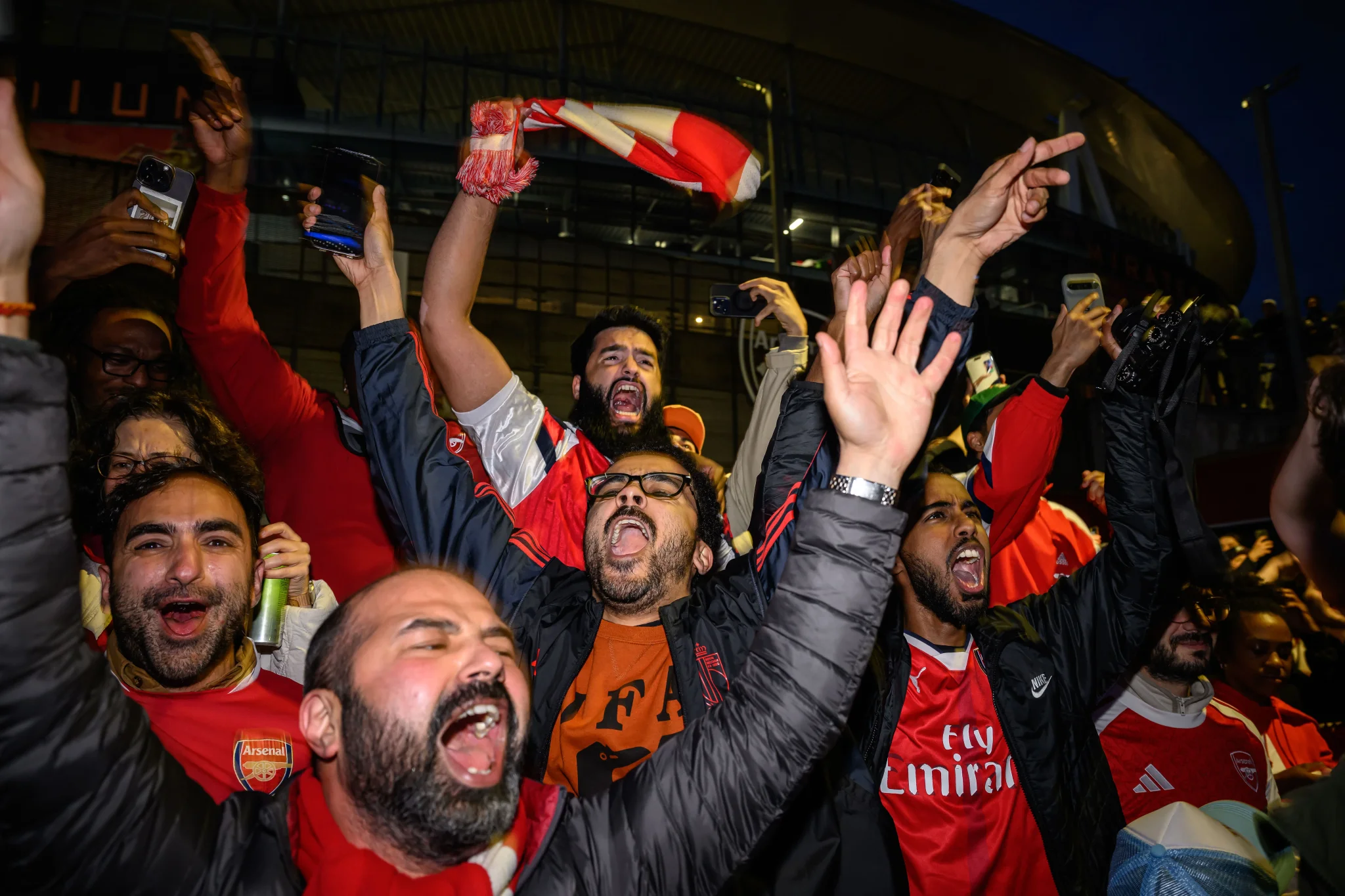 احتفال حماسي لجماهير Arsenal في شمال لندن بعد فوز الفريق بلقب الدوري الإنجليزي الممتاز، مع رفع الأعلام والهتافات.