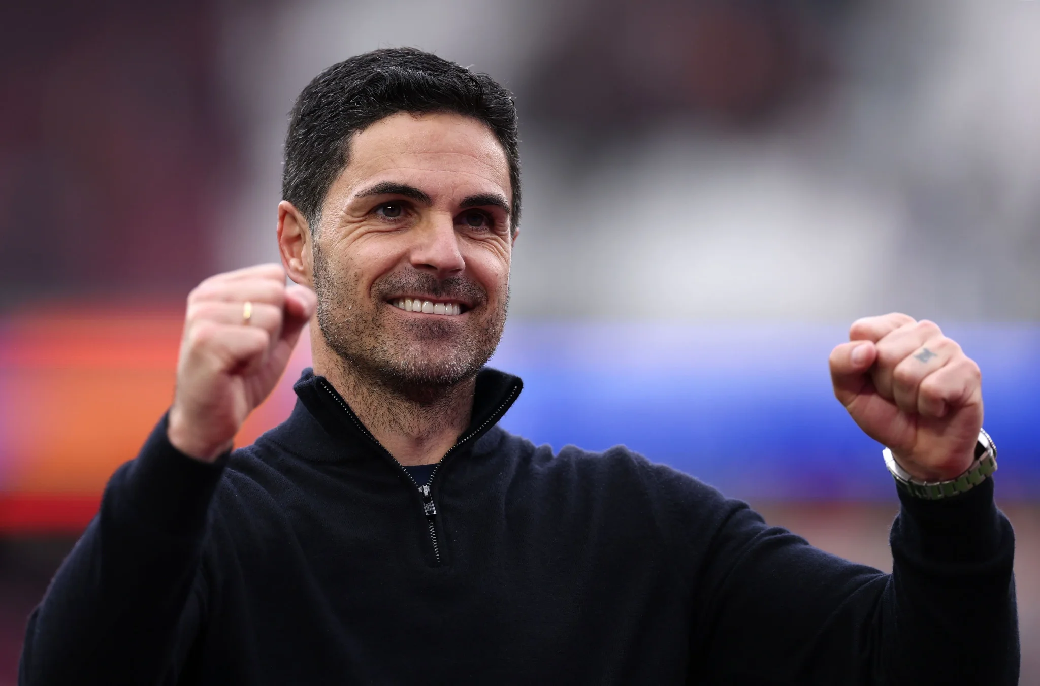 مدرب Arsenal، ميكيل أرتيتا، مبتسمًا ويرفع قبضته في إشارة للاحتفال، يعكس روح التفاؤل والتغيير في النادي بعد سنوات من التحديات.