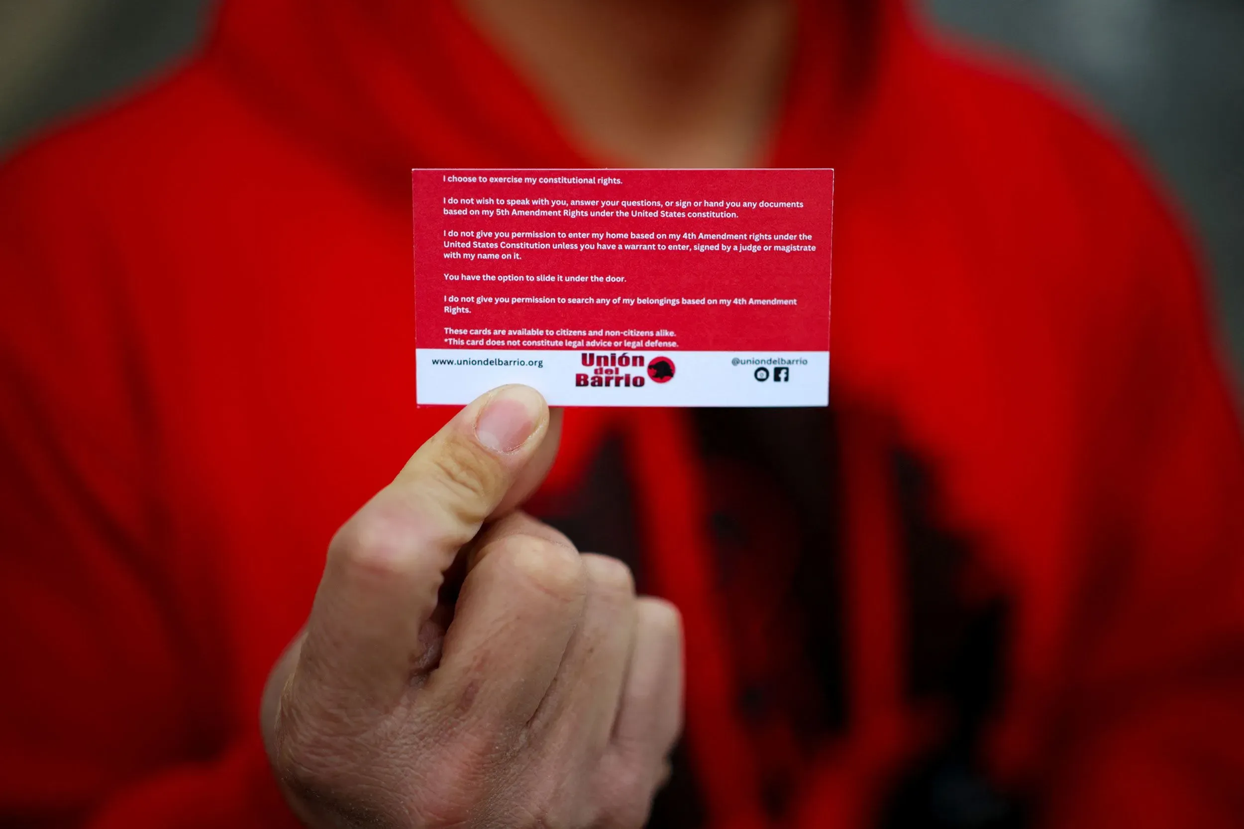 بطاقة حقوق دستورية تحمل نصوصًا تتعلق بالحقوق القانونية، ممسوكه بيد شخص يرتدي سترة حمراء، تعكس القلق من الترحيل.