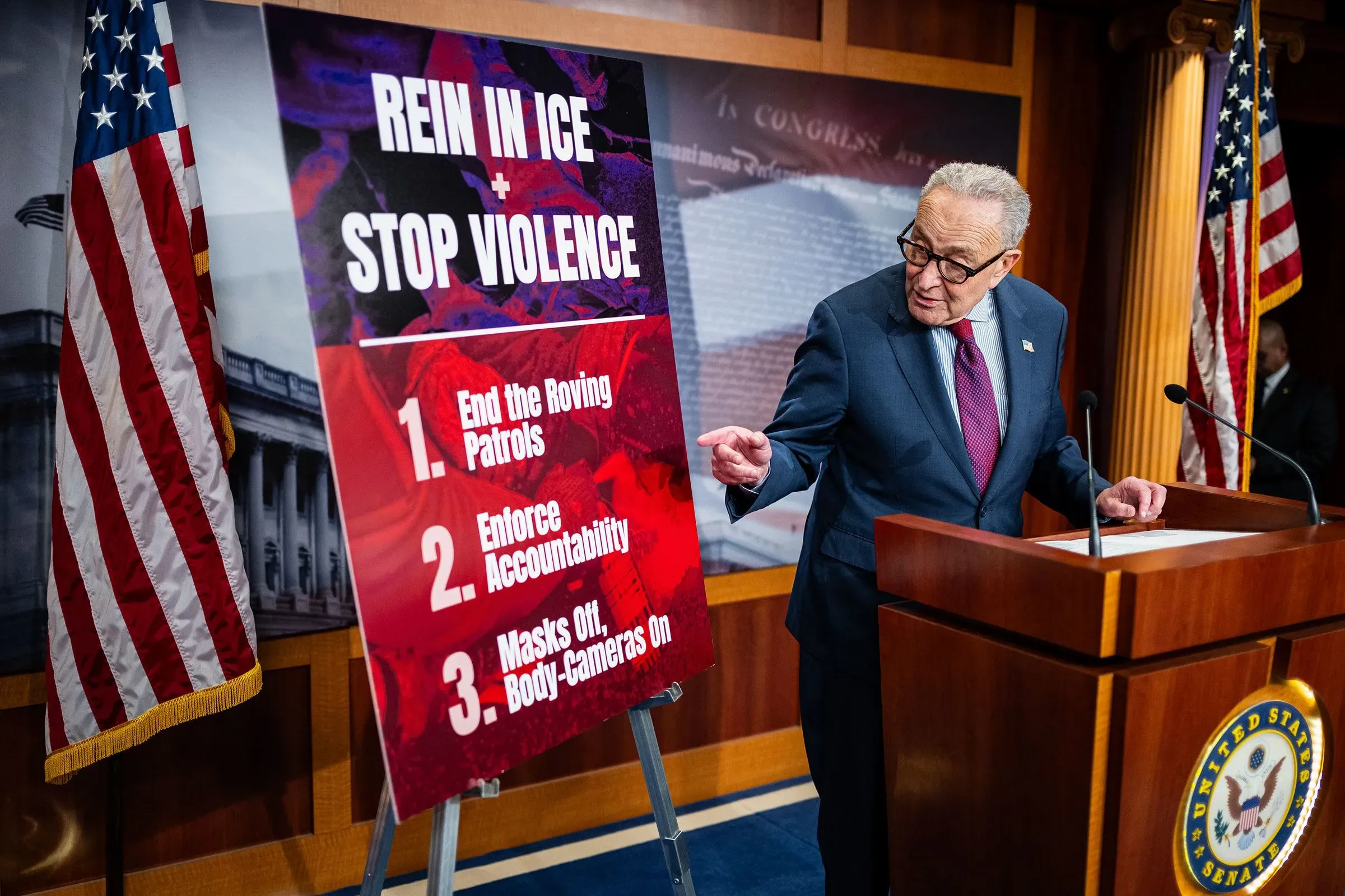 مشرع أمريكي يتحدث أمام لافتة تطالب بإنهاء الدوريات الجوالة وتعزيز المساءلة في تطبيق قوانين الهجرة.
