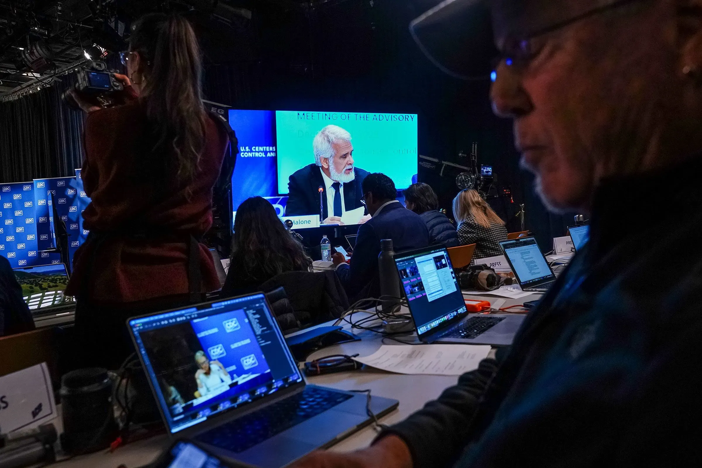 اجتماع في مراكز السيطرة على الأمراض والوقاية منها، حيث يظهر المتحدث الرئيسي على الشاشة بينما يركز الحضور على ملاحظاتهم وأجهزتهم الإلكترونية.