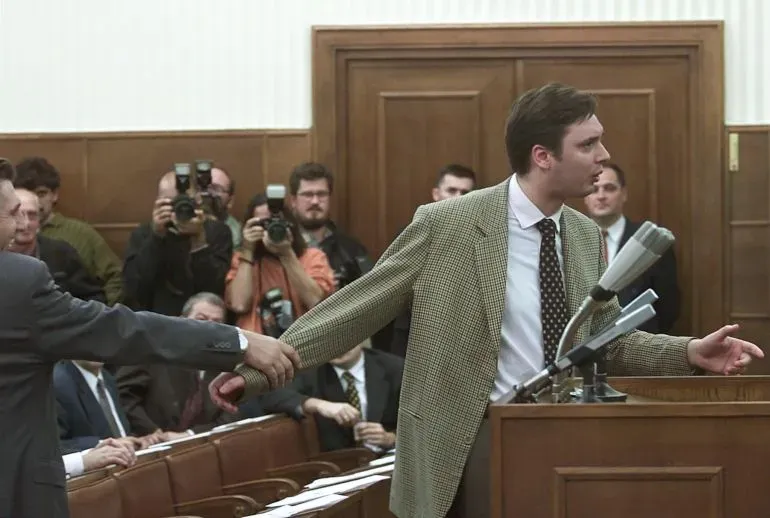 مشهد من جلسة برلمانية يظهر ألكسندر فوسيتش يتحدث بحماس، بينما يحاول شخص آخر جذبه بعيدًا. يحيط به مصورون وصحفيون.