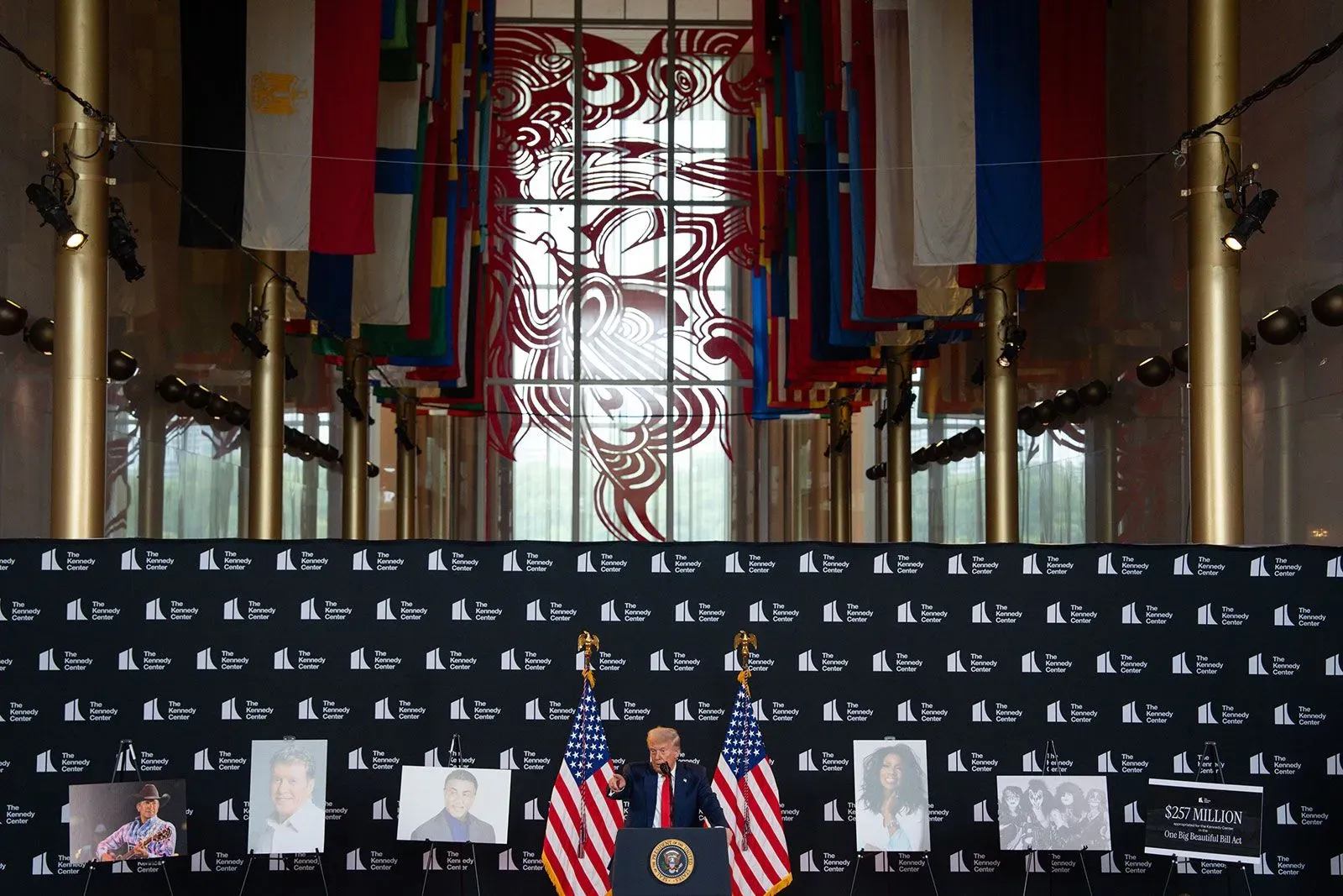 ترامب يتحدث في مركز كينيدي، محاطًا بأعلام دولية وصور المكرمين. الحدث يبرز تسييس الفنون وتأثير الثقافة الشعبية.