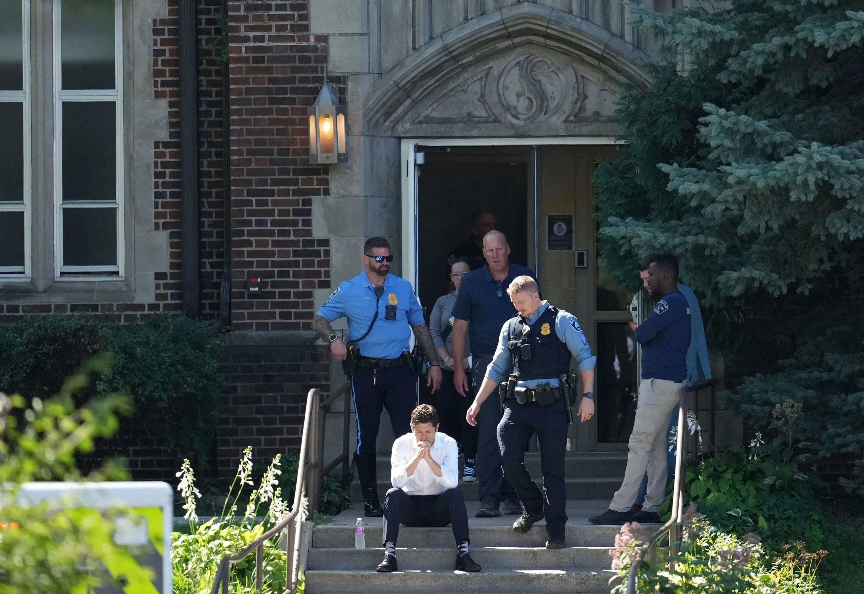 طفل يجلس على درجات كنيسة البشارة في مينيابوليس، محاط برجال الشرطة، بعد حادث إطلاق نار مأساوي أثناء قداس المدرسة.