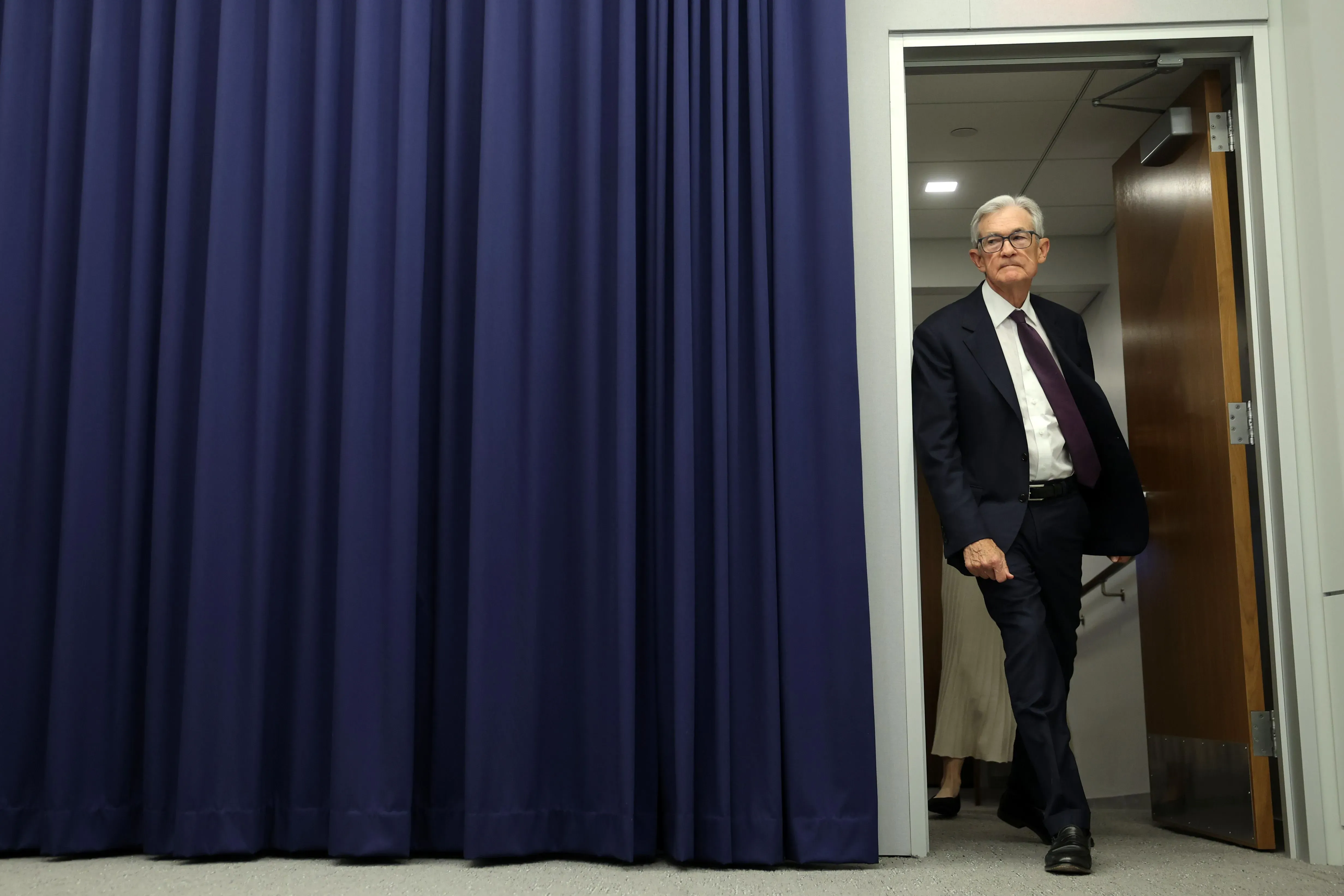 رئيس الاحتياطي الفيدرالي جيروم باول يغادر غرفة مؤتمرات، مما يعكس الضغوط السياسية المتزايدة على الإدارة الحالية.