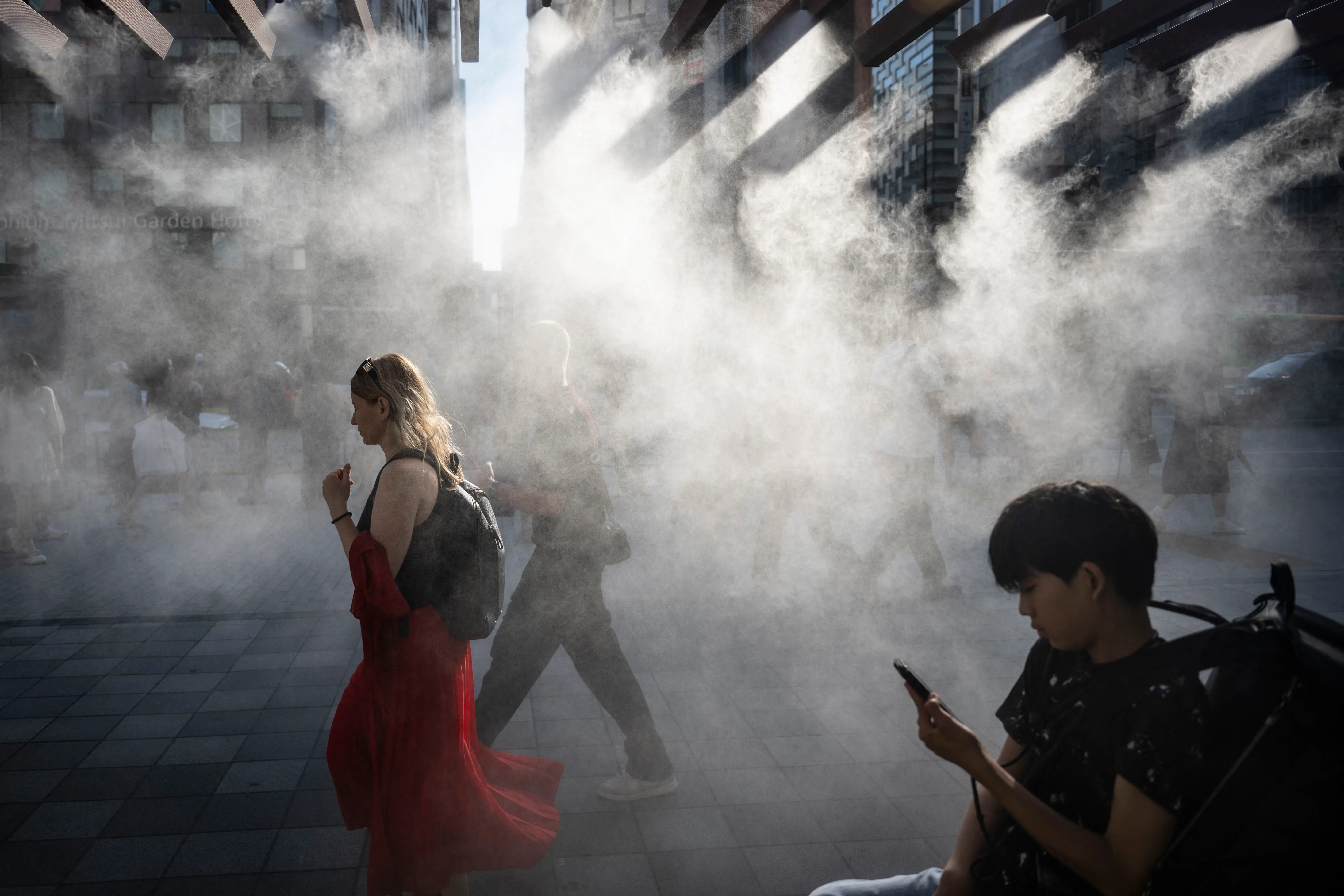 صورة تظهر أشخاصًا يسيرون في منطقة حضرية تحت تأثير الضباب المائي، مما يخفف من حرارة الصيف الشديدة في اليابان.