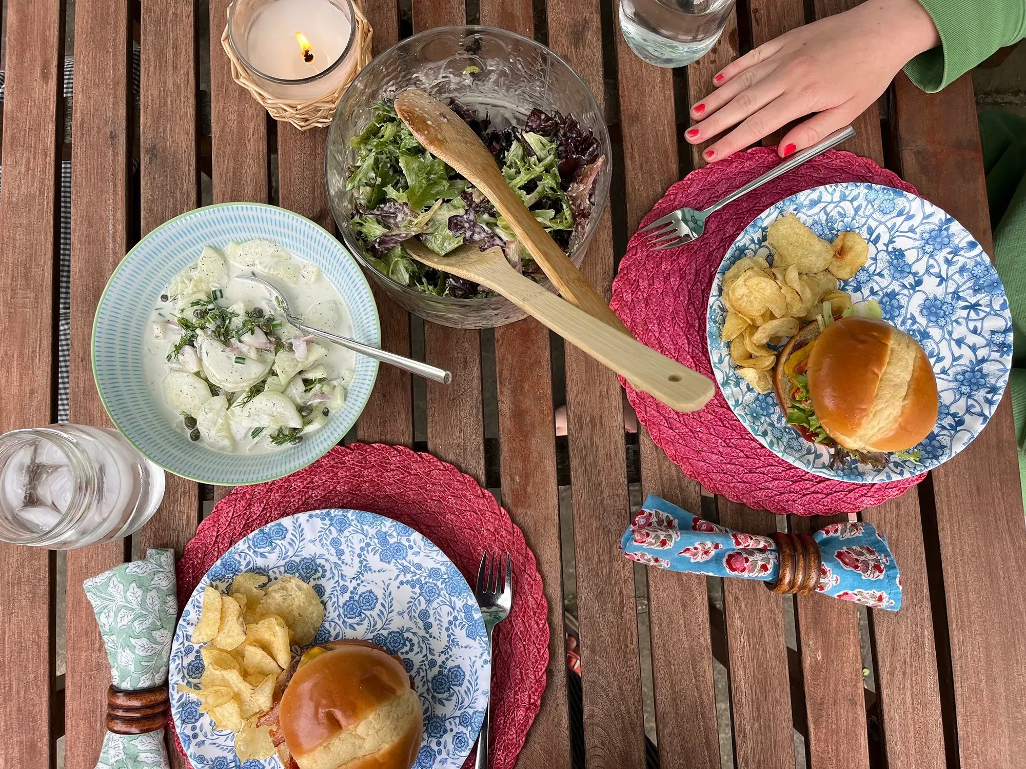 وجبة شهية تتكون من سلاطة وخبز برغر مع رقائق البطاطس، موضوعة على طاولة خشبية مع زجاجة ماء وشمعة مضاءة.