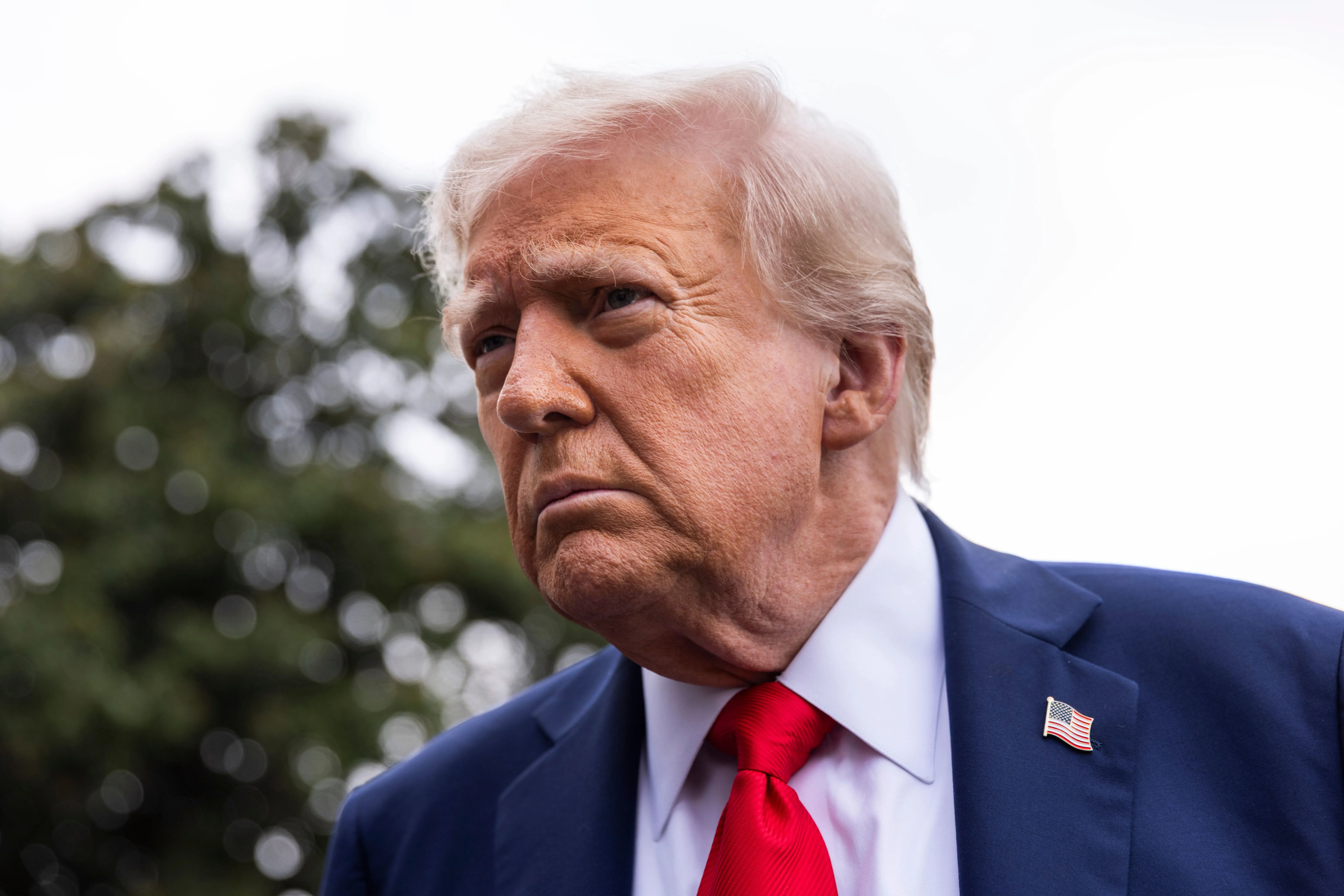 صورة لدونالد ترامب، مرتديًا بدلة زرقاء وربطة عنق حمراء، ينظر بتعبير جاد، مما يعكس التوترات السياسية الأخيرة في الولايات المتحدة.