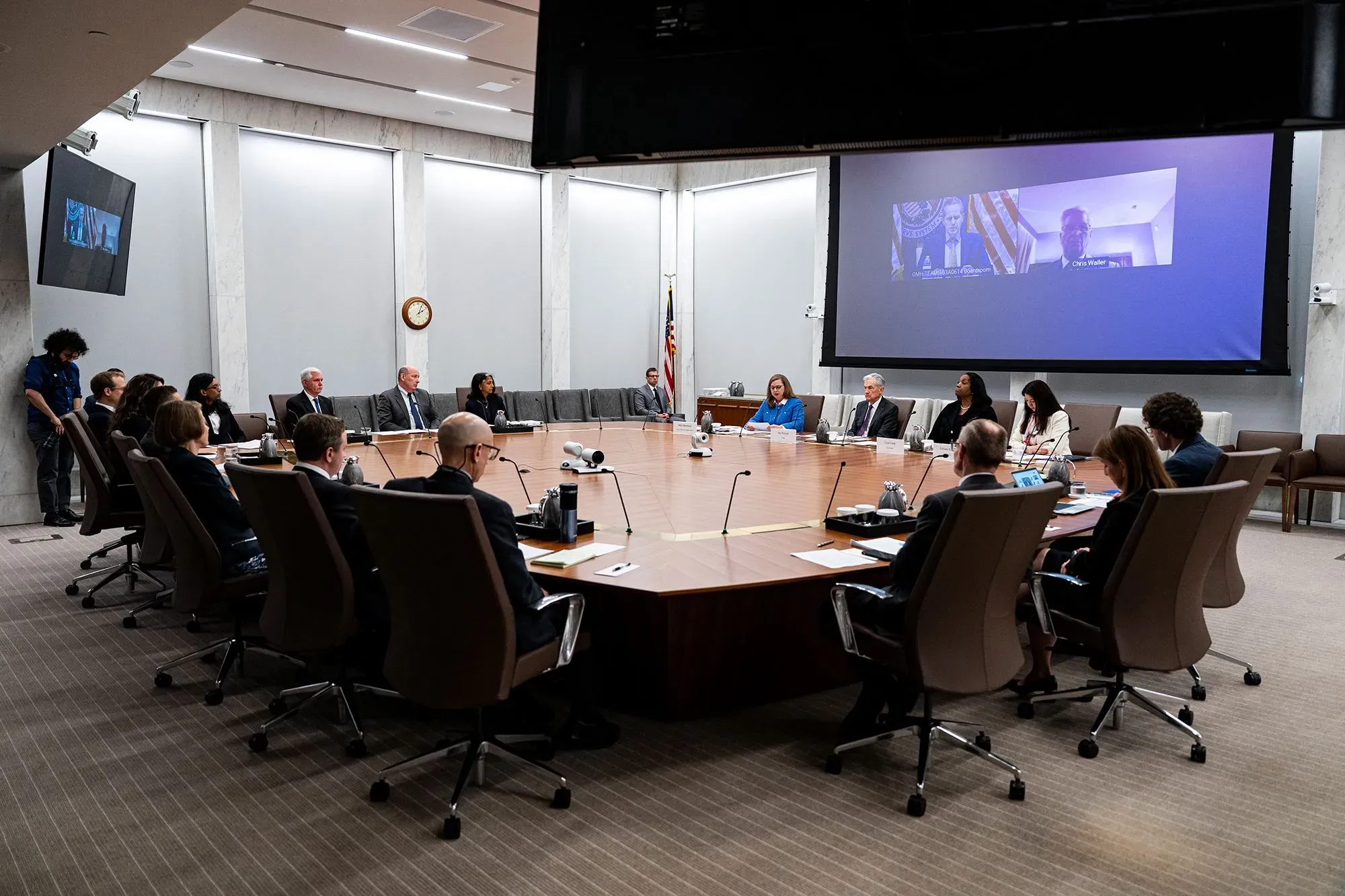 اجتماع لمجلس الاحتياطي الفيدرالي، حيث يجلس الأعضاء حول طاولة مستديرة، مع عرض تقديمي على الشاشة.