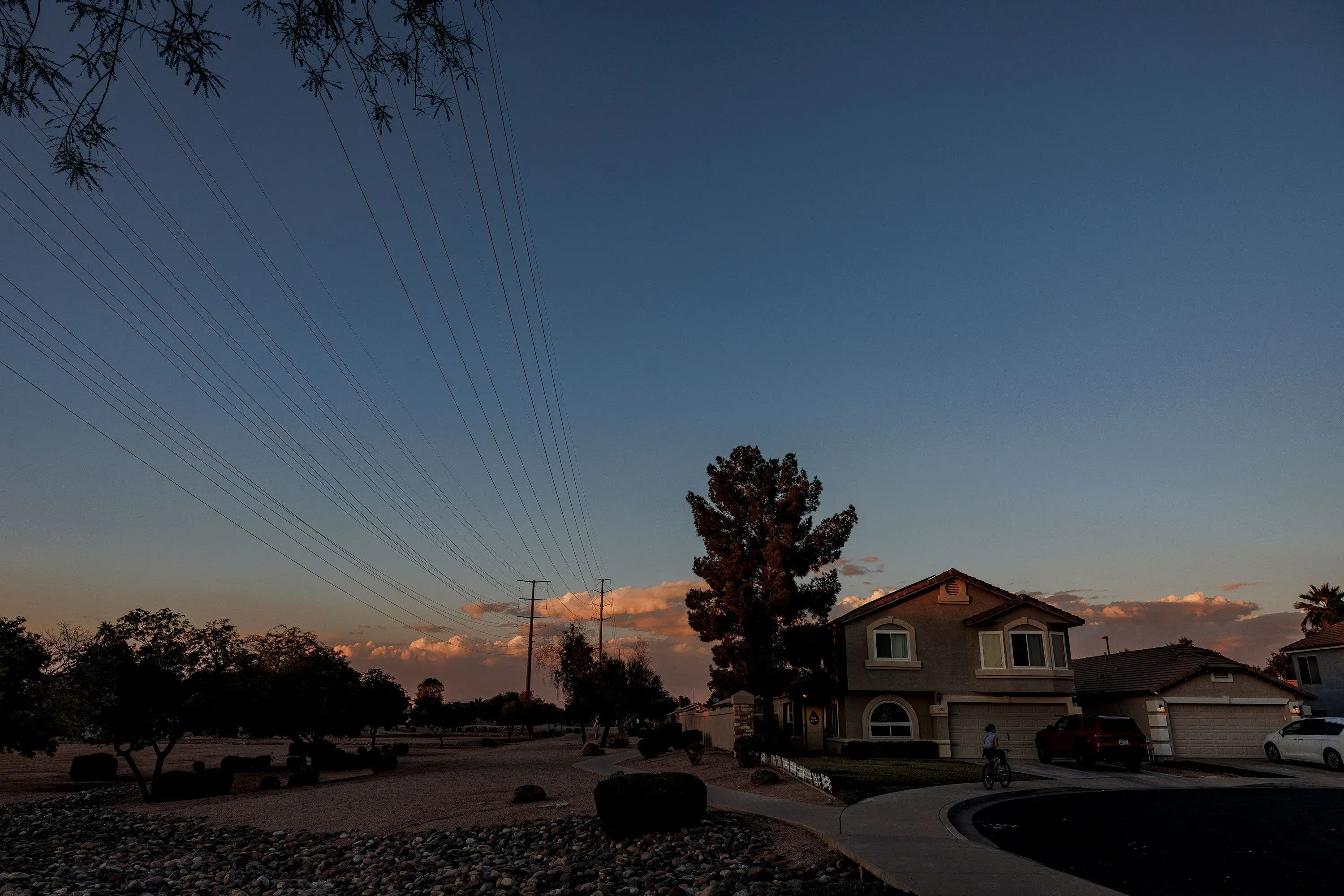 منظر لغروب الشمس فوق حي سكني في تشاندلر، أريزونا، مع خطوط كهرباء وأشجار، يبرز القضايا البيئية والاقتصادية لمراكز البيانات.