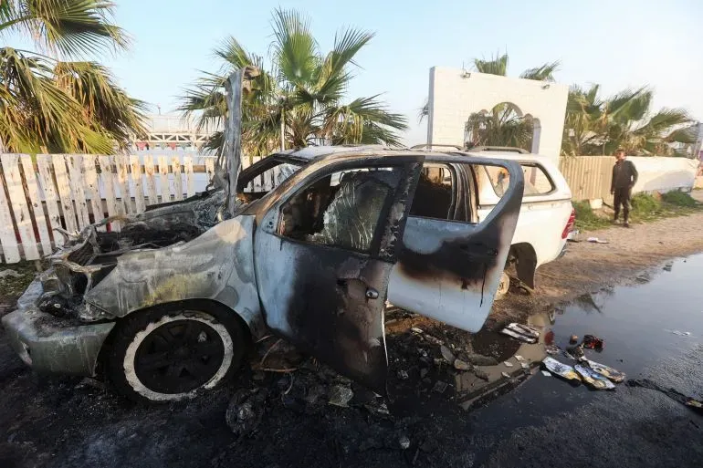 سيارة محترقة بجانب أشجار النخيل، تظهر آثار الحريق على الهيكل الخارجي، تعكس العنف المتزايد في الضفة الغربية.