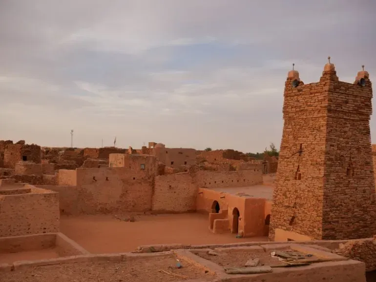 منظر لمدينة شنقيط القديمة في موريتانيا، تظهر فيها المباني التقليدية المصنوعة من الحجر والطين، مع برج مميز في الخلفية.