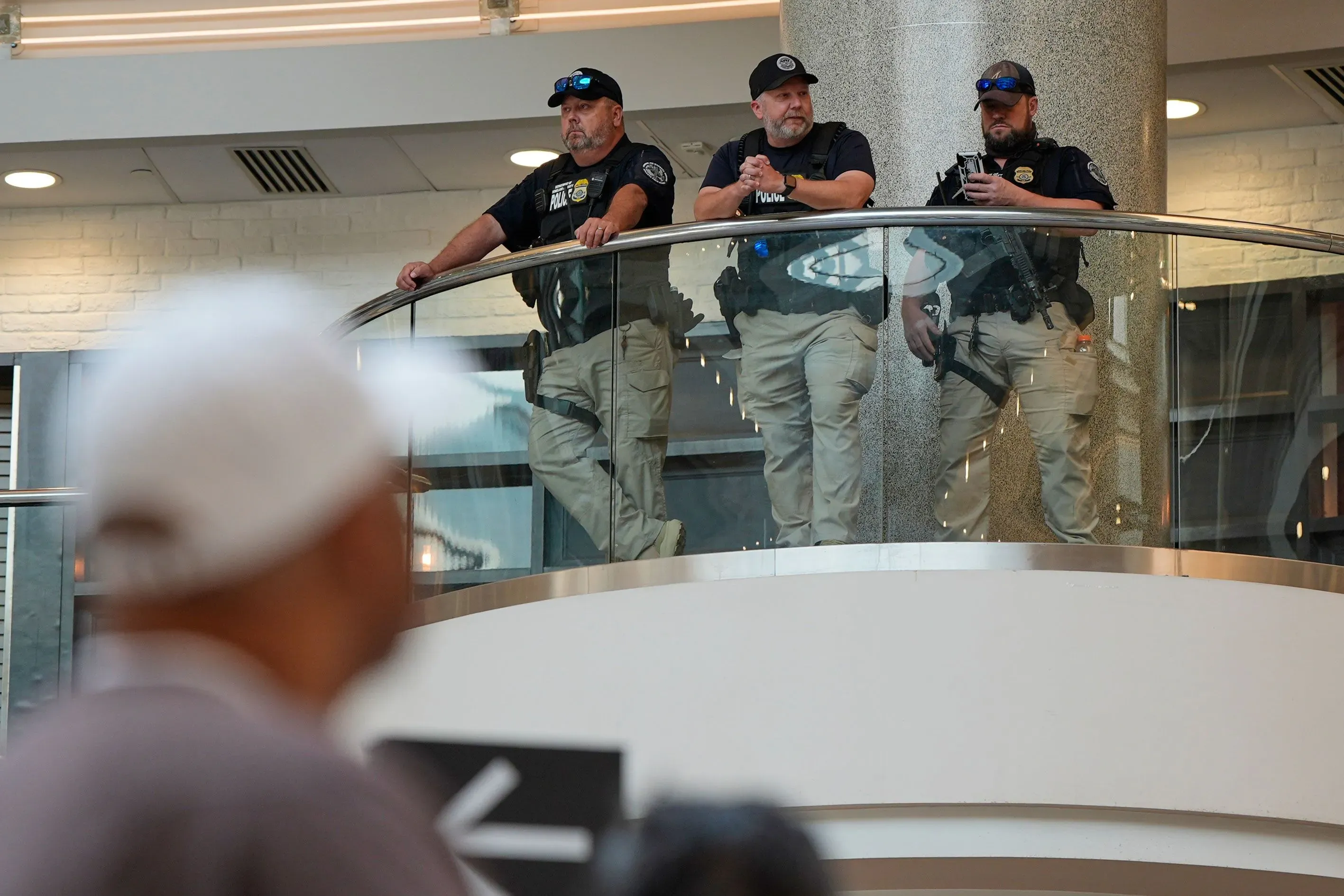 موظفو الهجرة والجمارك يراقبون المسافرين في مطار، بينما يظهر شخص في المقدمة. الصورة تعكس تأثير الإغلاق على السفر.