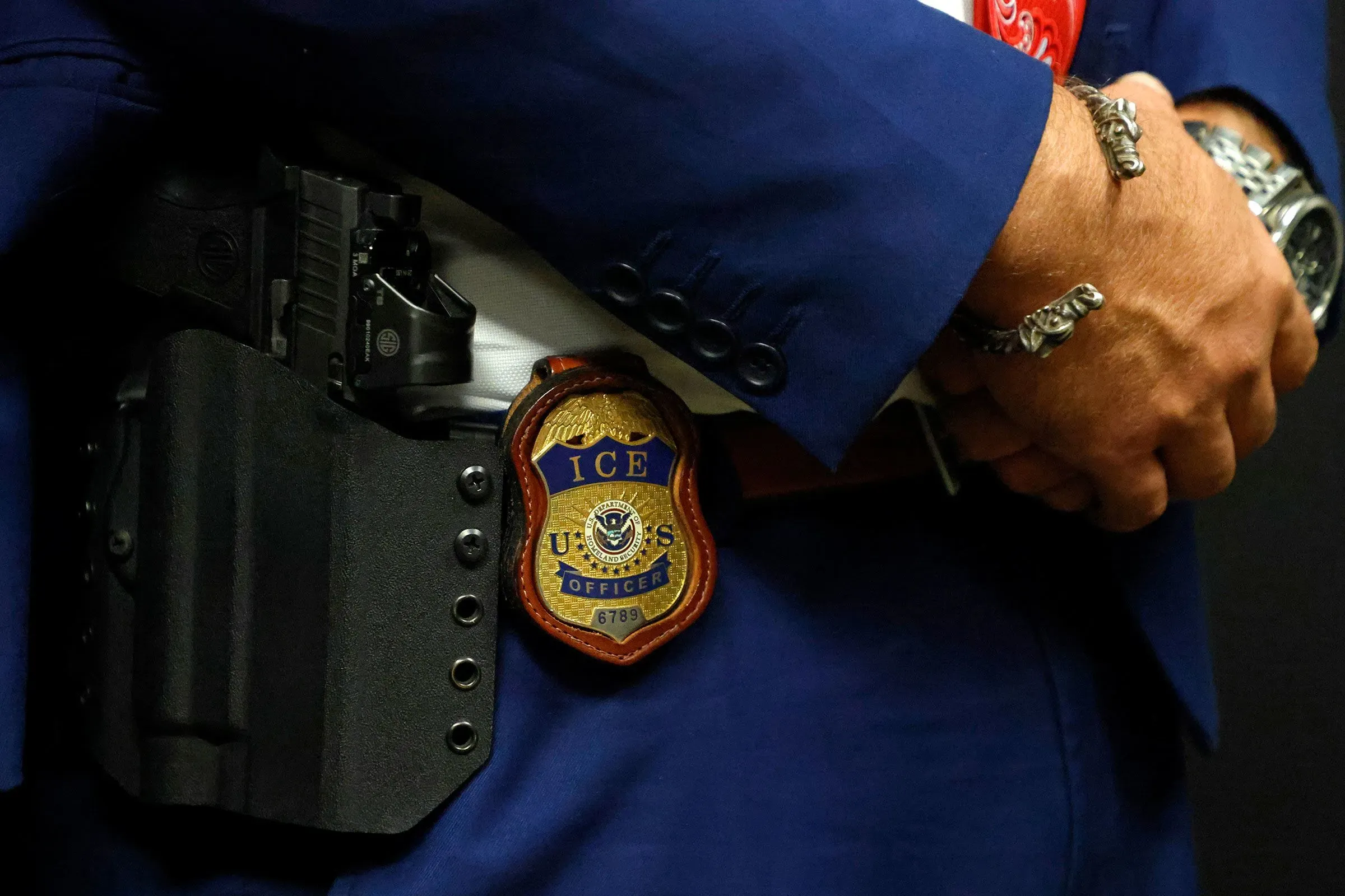 شعار ضابط إنفاذ قوانين الهجرة والجمارك الأمريكية مع مسدس في حزامه، يعكس قلة التدريب مقارنة بالوكالات الفيدرالية الأخرى.