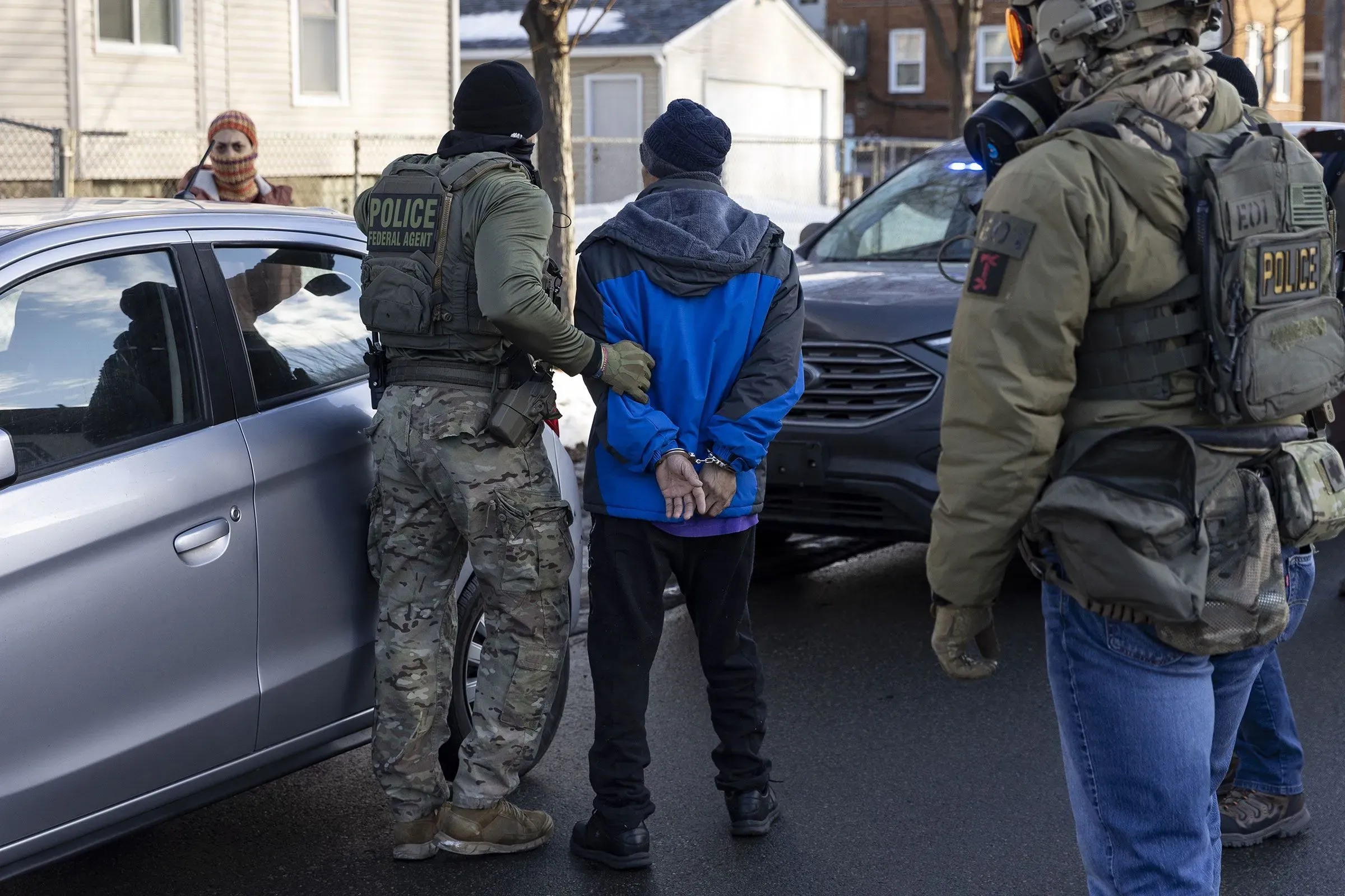 عملاء الهجرة والجمارك يعتقلون شخصًا في الشارع، مع استخدامهم للهواتف المحمولة لتوثيق العملية.