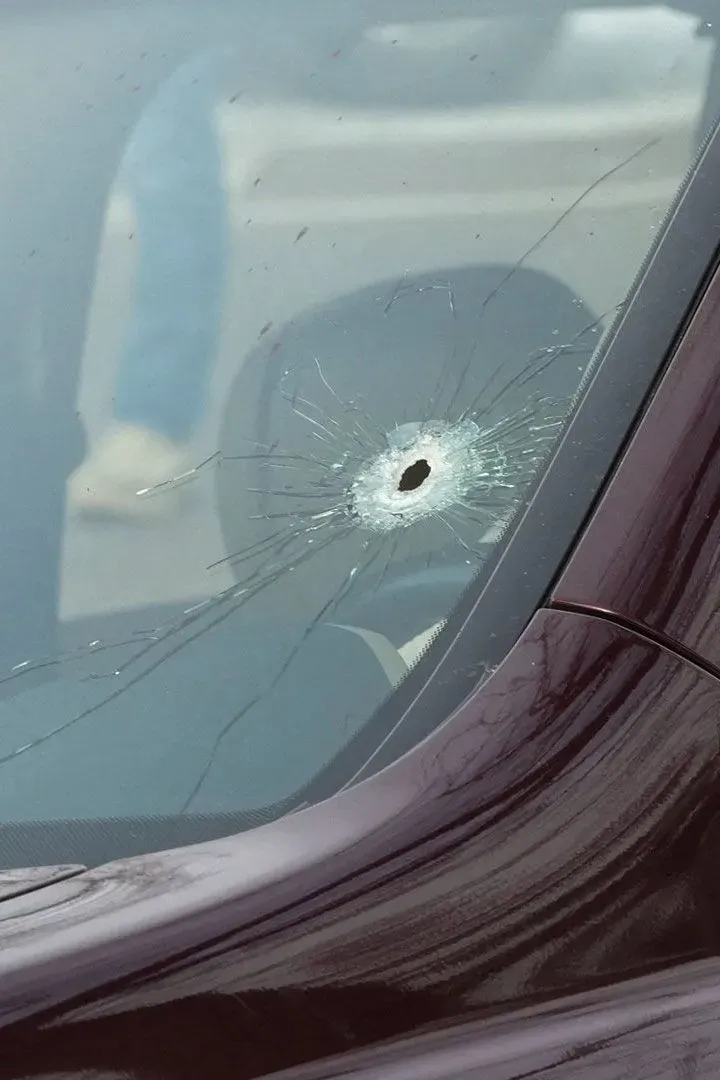ثقب في زجاج سيارة، يظهر آثار تحطم واضحة، مما يشير إلى حادثة عنف. يتماشى مع موضوع استخدام كاميرات الهواتف المحمولة في عمليات إنفاذ القانون.