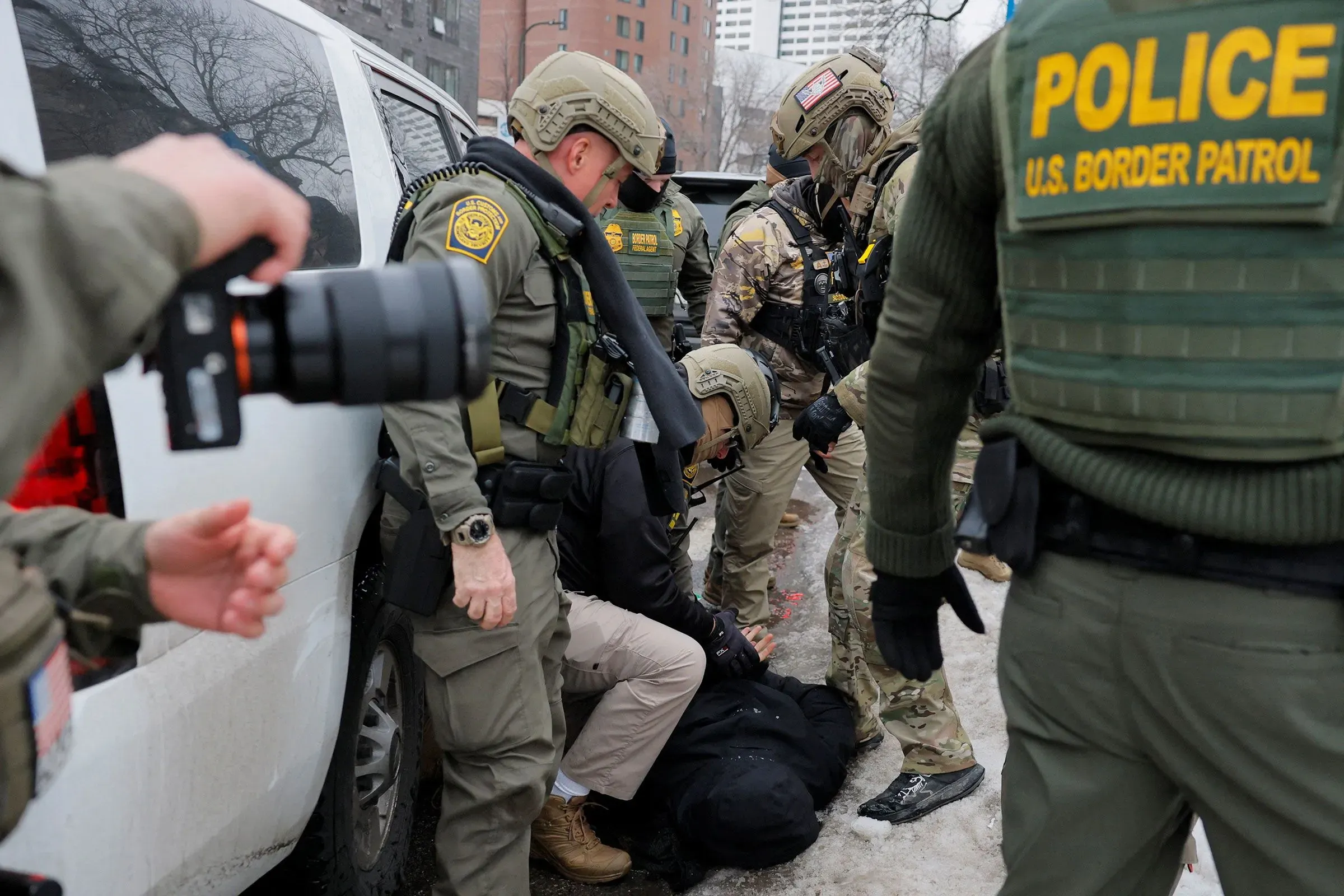 عملاء إنفاذ قوانين الهجرة والجمارك يستخدمون كاميرات الهواتف المحمولة أثناء عملية اعتقال، مما يبرز استخدام التكنولوجيا في الميدان.