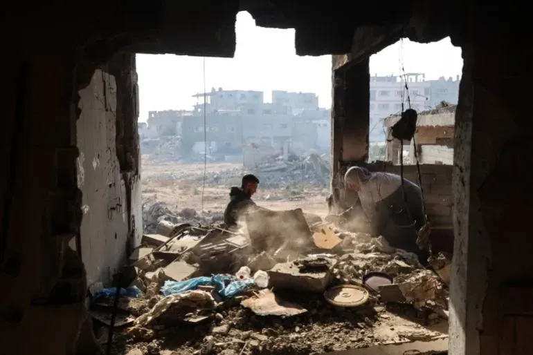 رجال يعملون على إزالة الأنقاض في غزة، مع خلفية من المباني المدمرة، تعكس آثار الحرب والدمار في المنطقة.