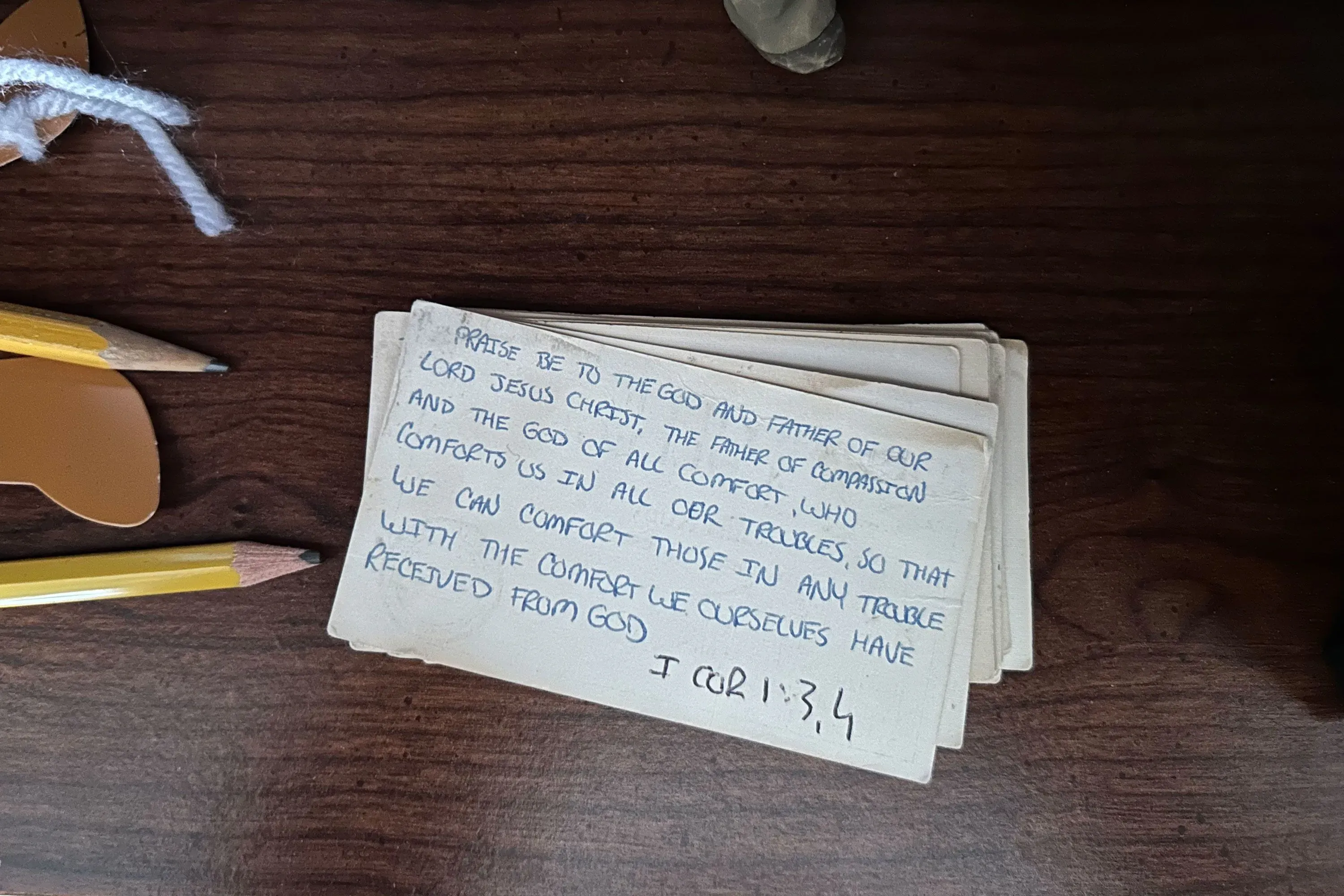 بطاقات مكتوبة تحتوي على نص ديني يتحدث عن التعزية والمساعدة في الأوقات الصعبة، مع أقلام رصاص وأشياء أخرى على سطح خشبي.