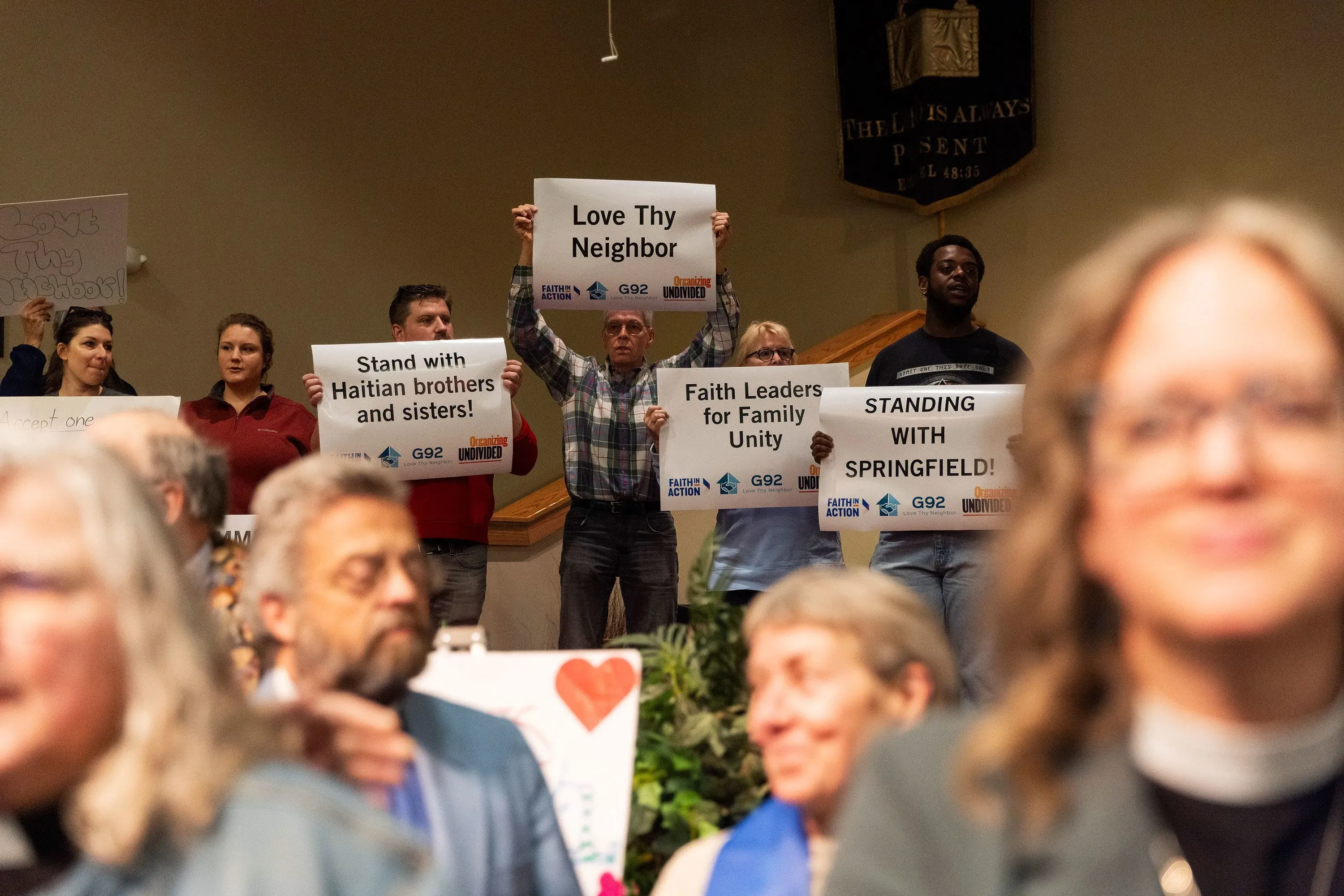مجموعة من المتظاهرين في كنيسة يحملون لافتات تدعو لدعم المهاجرين الهايتيين، مع التركيز على الوحدة العائلية والتضامن في سبرينغفيلد.