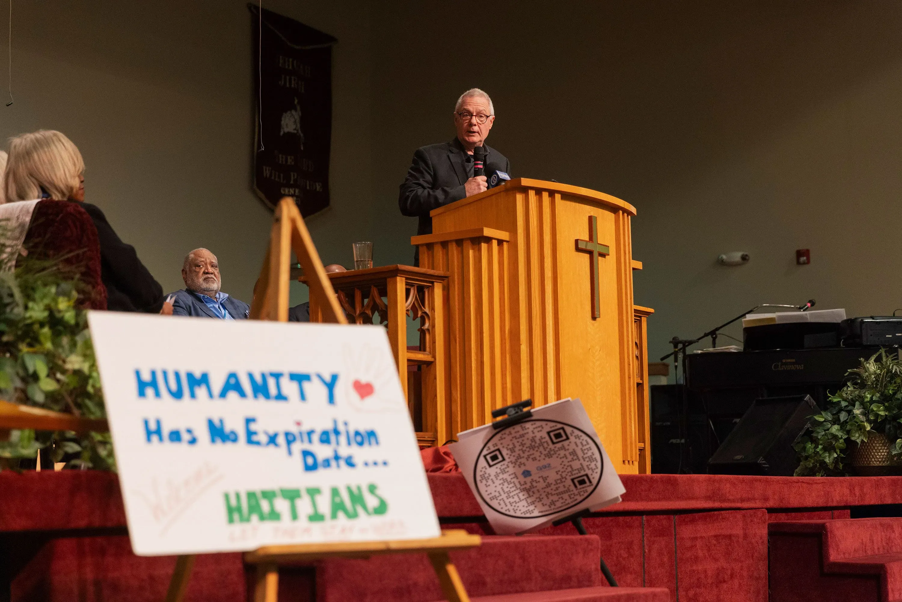 القس كارل روبي يلقي عظته في الكنيسة، مع لافتة تدعو إلى دعم الهايتيين، وسط أجواء من القلق بشأن التهديدات الأمنية.