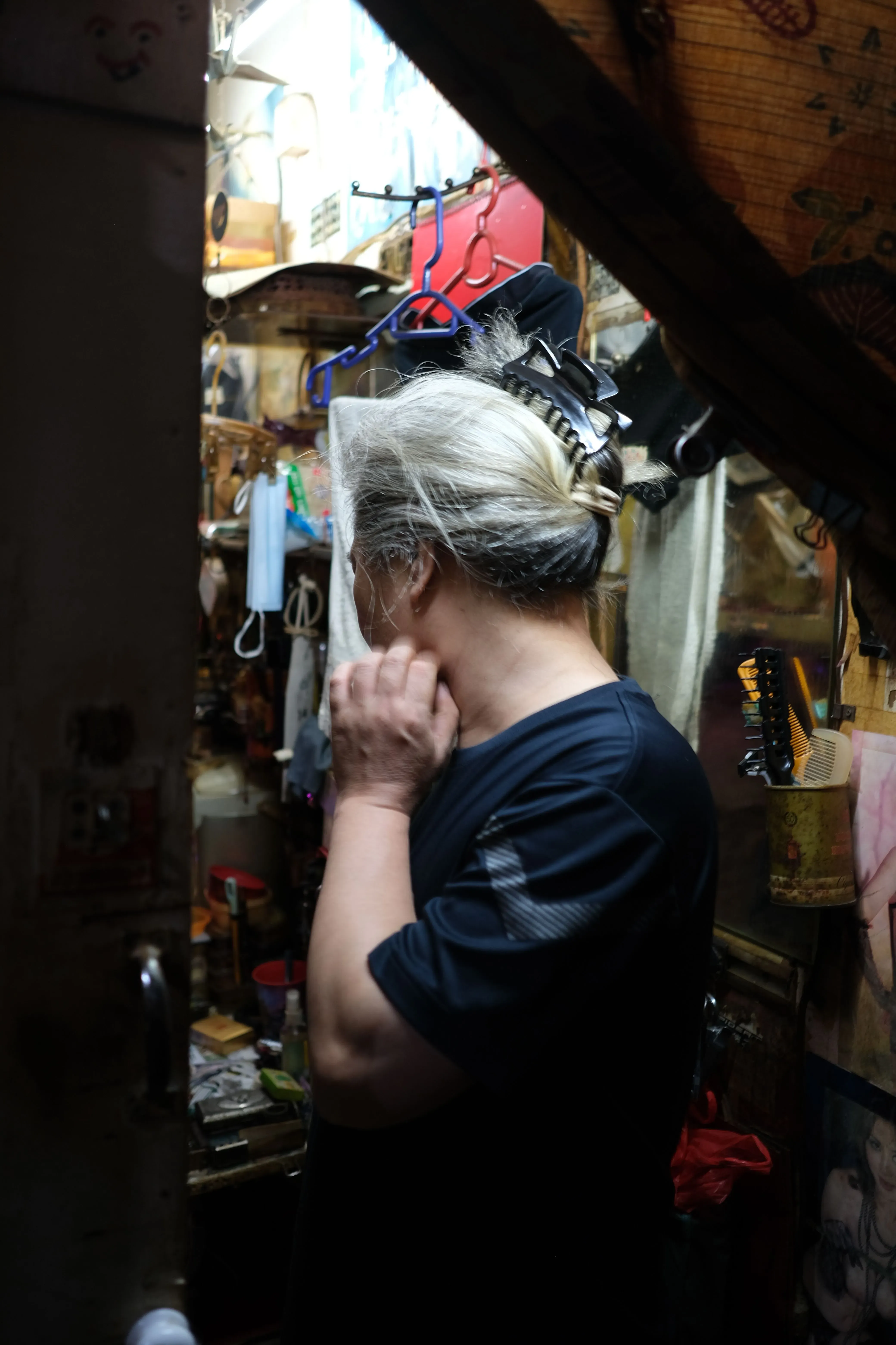 شخص يقف في غرفة صغيرة مزدحمة، محاط بأغراض شخصية، يعكس الظروف المعيشية الصعبة في هونغ كونغ.