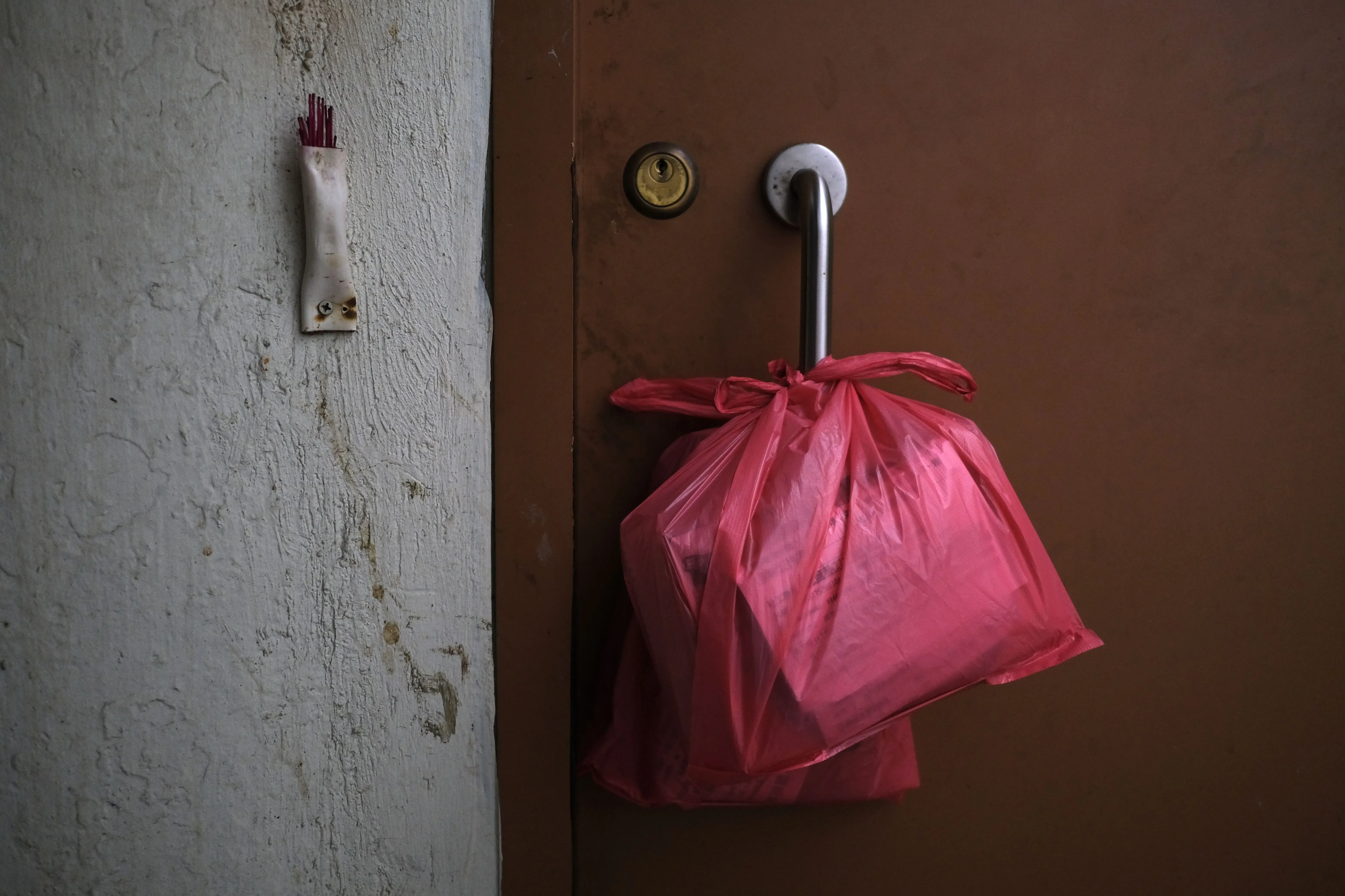 أكياس قمامة حمراء معلقة على مقبض باب شقة في هونغ كونغ، تعكس ظروف المعيشة الصعبة في المنازل الضيقة والمكتظة.