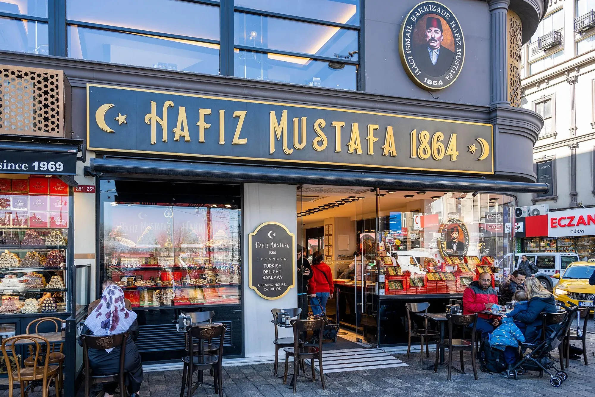 واجهة محل "هافز مصطفى 1864" في إسطنبول، تعرض مجموعة متنوعة من الحلوى التركية، مع زبائن يجلسون في الخارج.