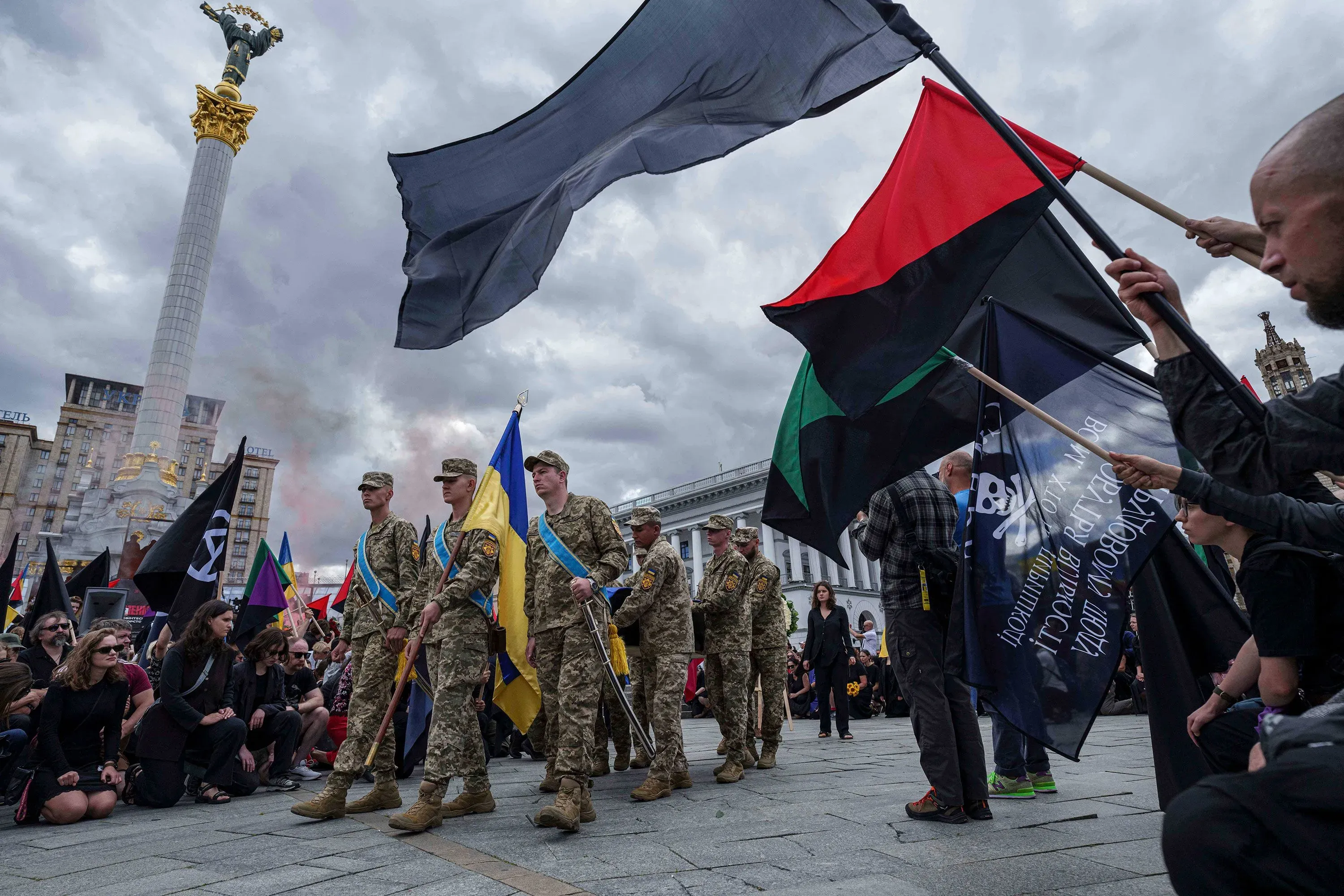 جنود أوكرانيون يرتدون الزي العسكري يقفون في ميدان الاستقلال وسط حشود من المتظاهرين، مع أعلام أوكرانية وأعلام أخرى ترفرف في الهواء.