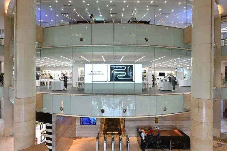 مركز تسوق حديث في إندونيسيا يظهر انخفاض عدد المتسوقين، مع وجود لافتات إعلانات وعرض لمستحضرات التجميل.