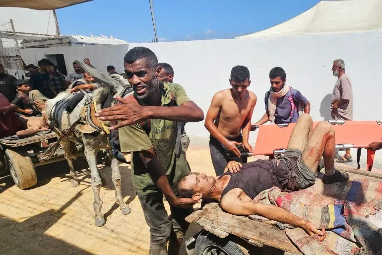 تظهر الصورة رجالًا فلسطينيين ينقلون مصابًا على عربة، وسط أجواء من الفوضى بعد وقوع أحداث عنف في غزة.