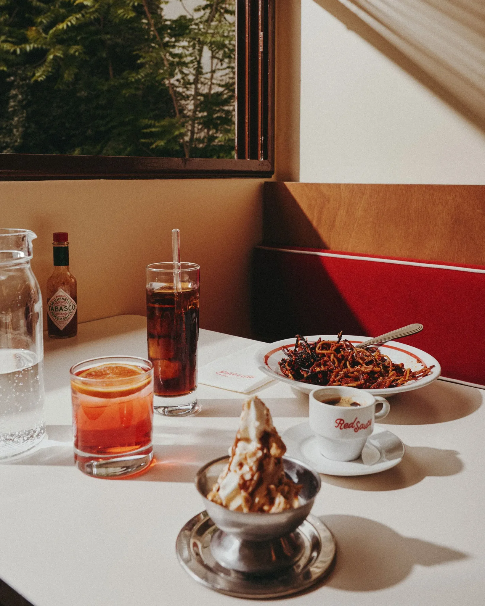 مشروبات متنوعة وحلوى مثلجة على طاولة مطعم Red Sauce في باريس مع أجواء دافئة وإضاءة طبيعية تعكس تجربة الطعام الأمريكي في فرنسا.