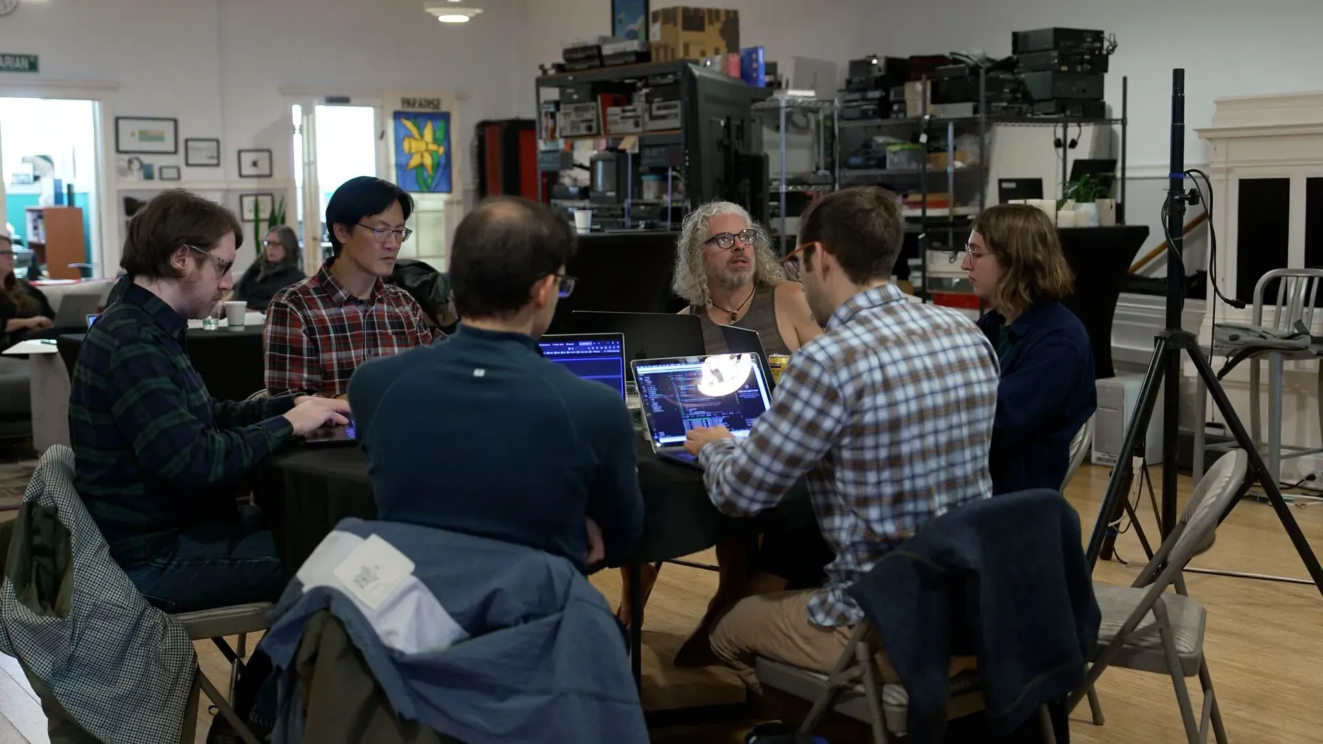 مجموعة من الأشخاص يجلسون حول طاولة، يعملون على أجهزة الكمبيوتر المحمولة في بيئة تعاونية، تعكس جهود أرشيف الإنترنت للحفاظ على تاريخ الويب.