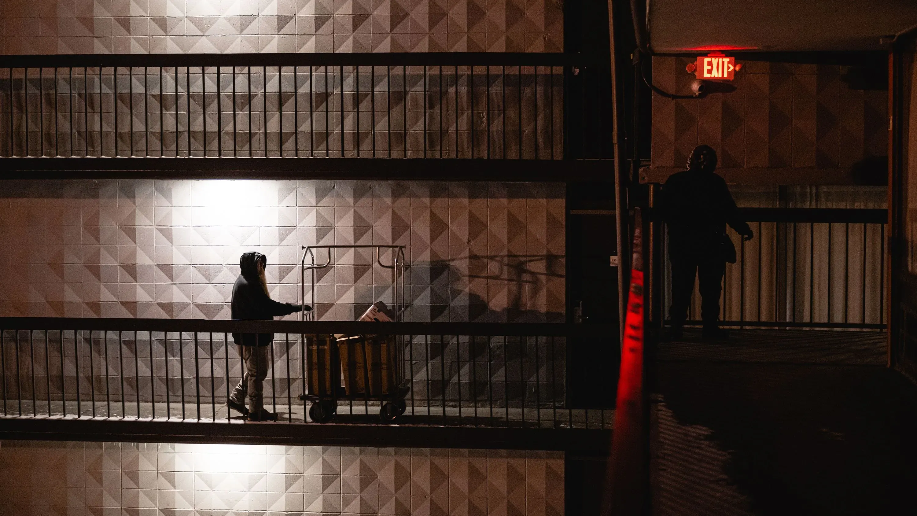 امرأة تدفع عربة تسوق في ممر مظلم، تعكس مشهد الحياة اليومية للأشخاص الذين يعيشون في ظروف صعبة وغير مستقرة.