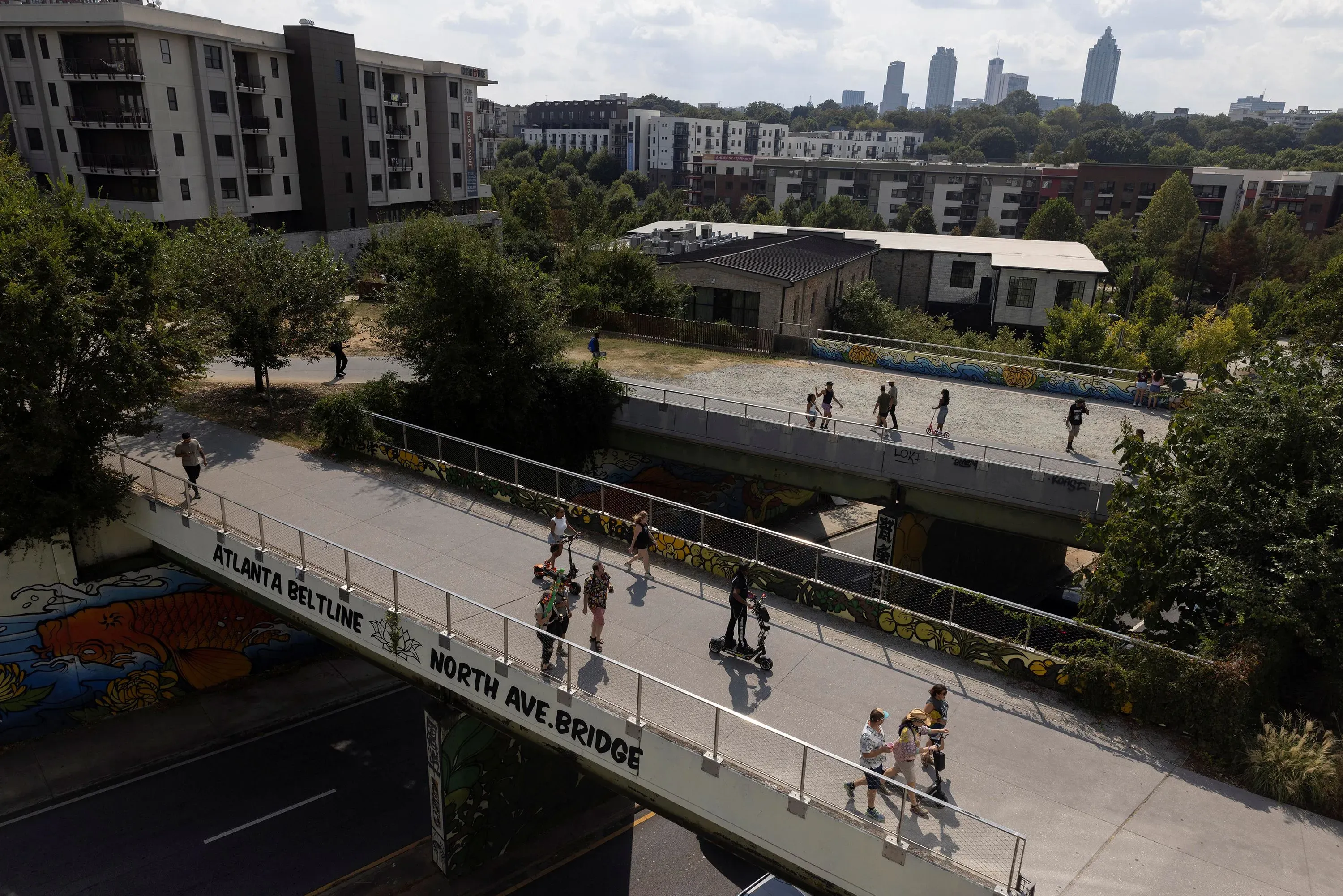 منظر عام لجسر في أتلانتا يمر فوق طريق، حيث يسير الناس في اتجاهات مختلفة، مع خلفية لمباني سكنية وأشجار.