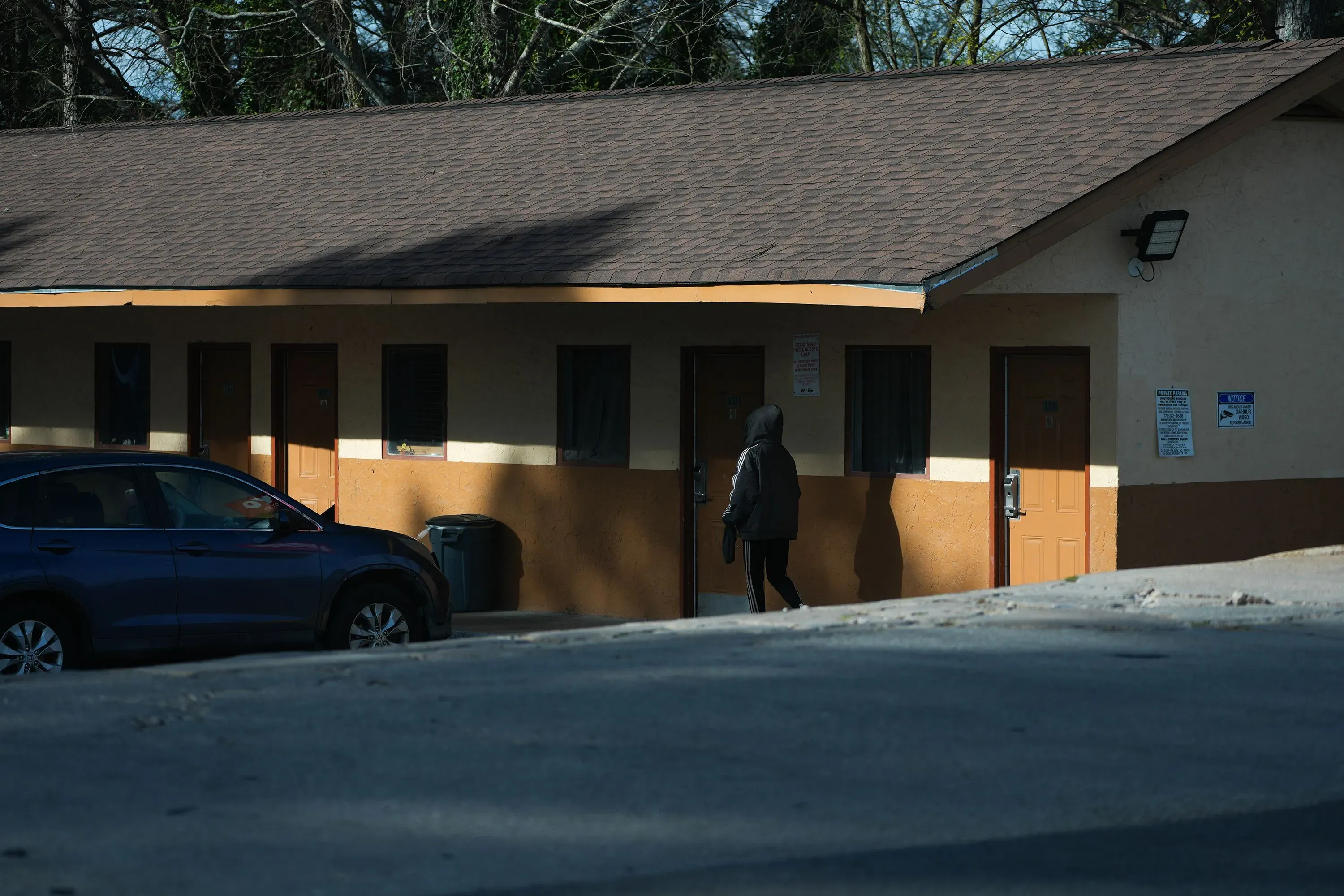 امرأة ترتدي سترة داكنة تسير نحو مدخل فندق منخفض التكلفة، تعكس واقع عدم الاستقرار السكني الذي يعاني منه الكثيرون.