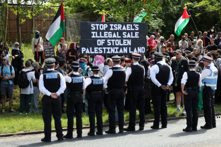 محتجون يحملون لافتة تطالب بوقف بيع الأراضي الفلسطينية المسروقة، بينما يقف عناصر الشرطة أمامهم خلال فعالية في لندن.