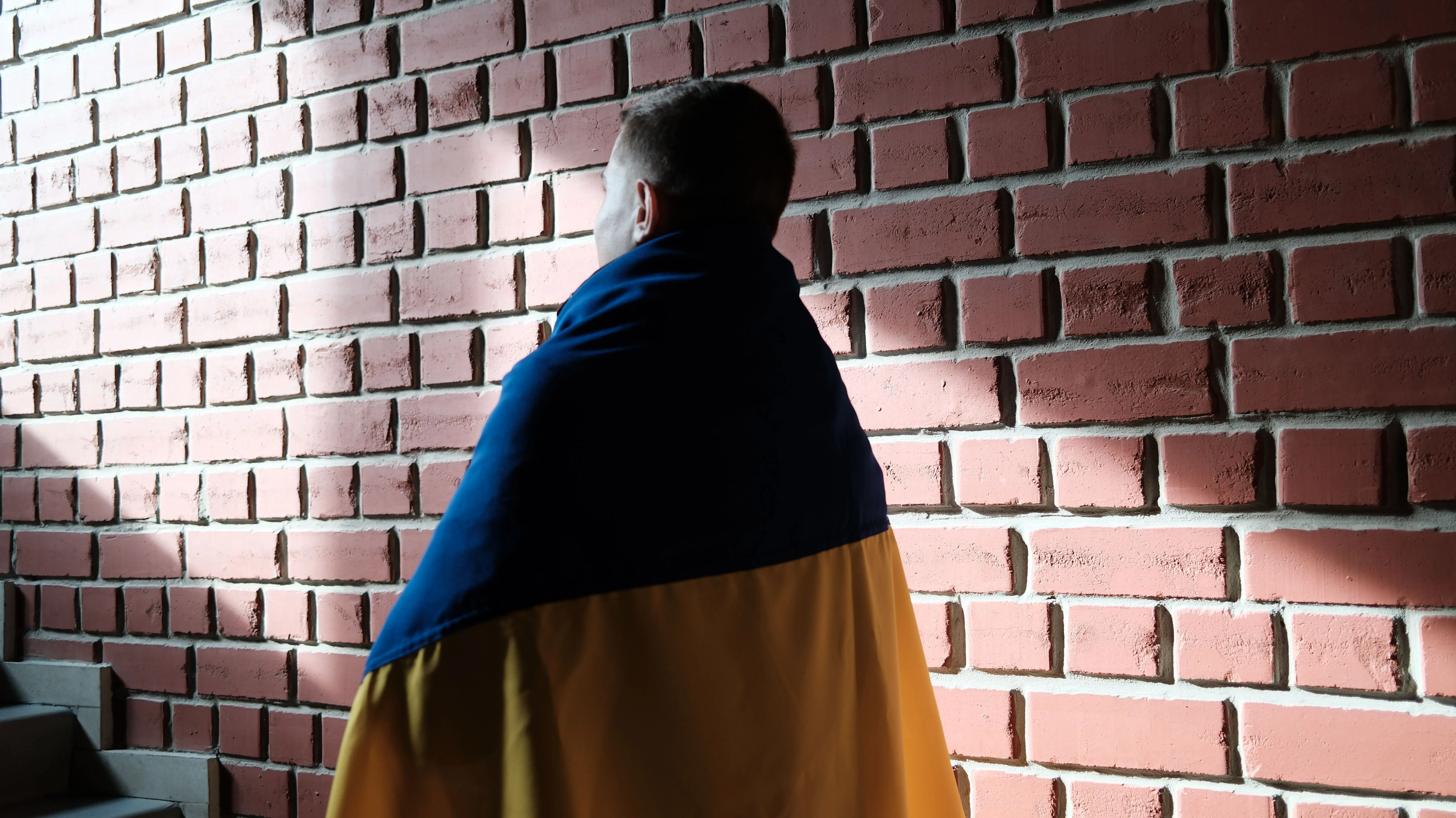 شاب مغطى بعلم أوكرانيا يقف أمام جدار من الطوب، يعبر عن الأمل بعد عودته من روسيا إلى أوكرانيا.