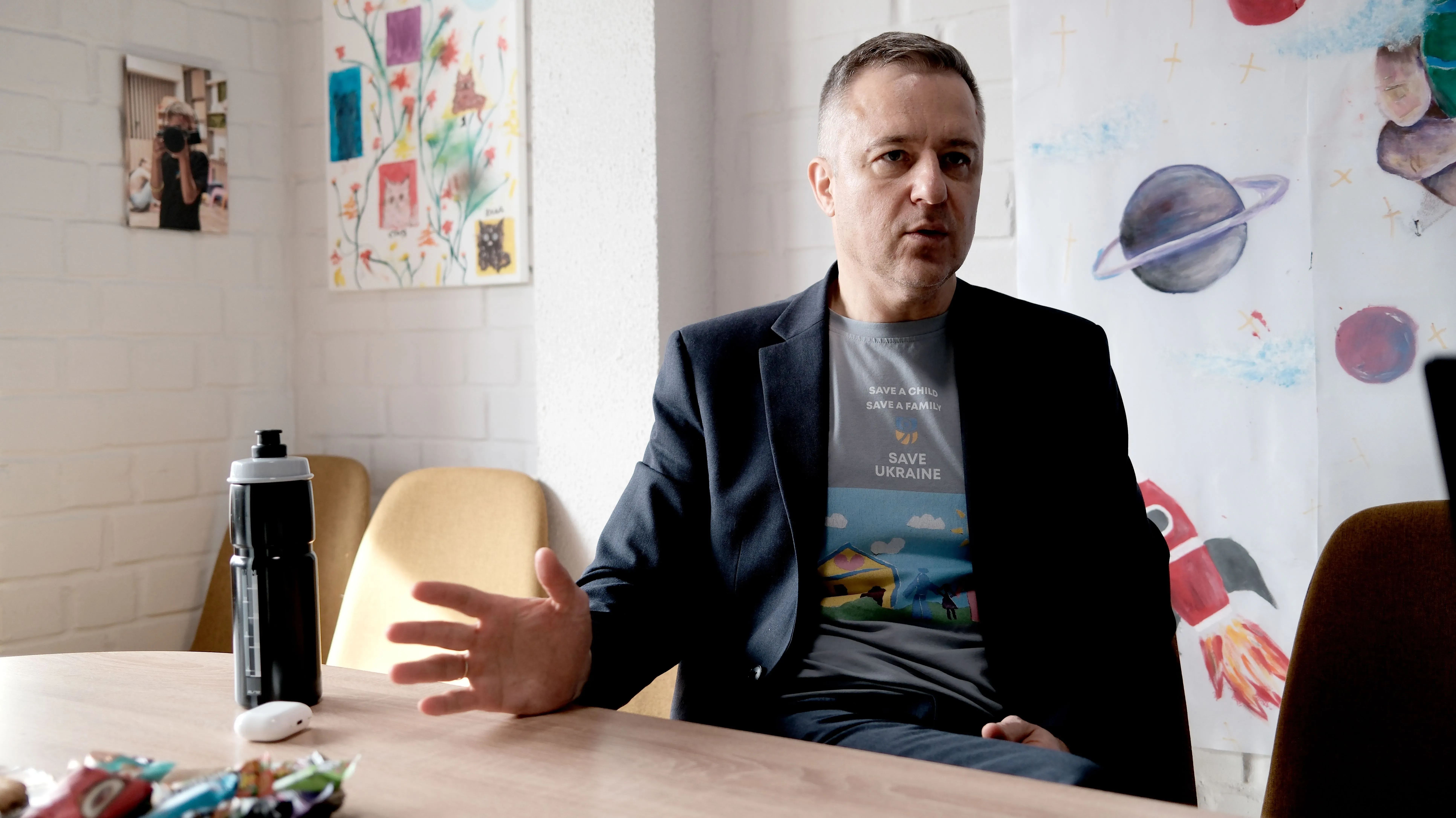 مؤسس منظمة "أنقذوا أوكرانيا" يتحدث عن جهود إنقاذ الأطفال الأوكرانيين العالقين في روسيا، مع خلفية فنية ملونة.