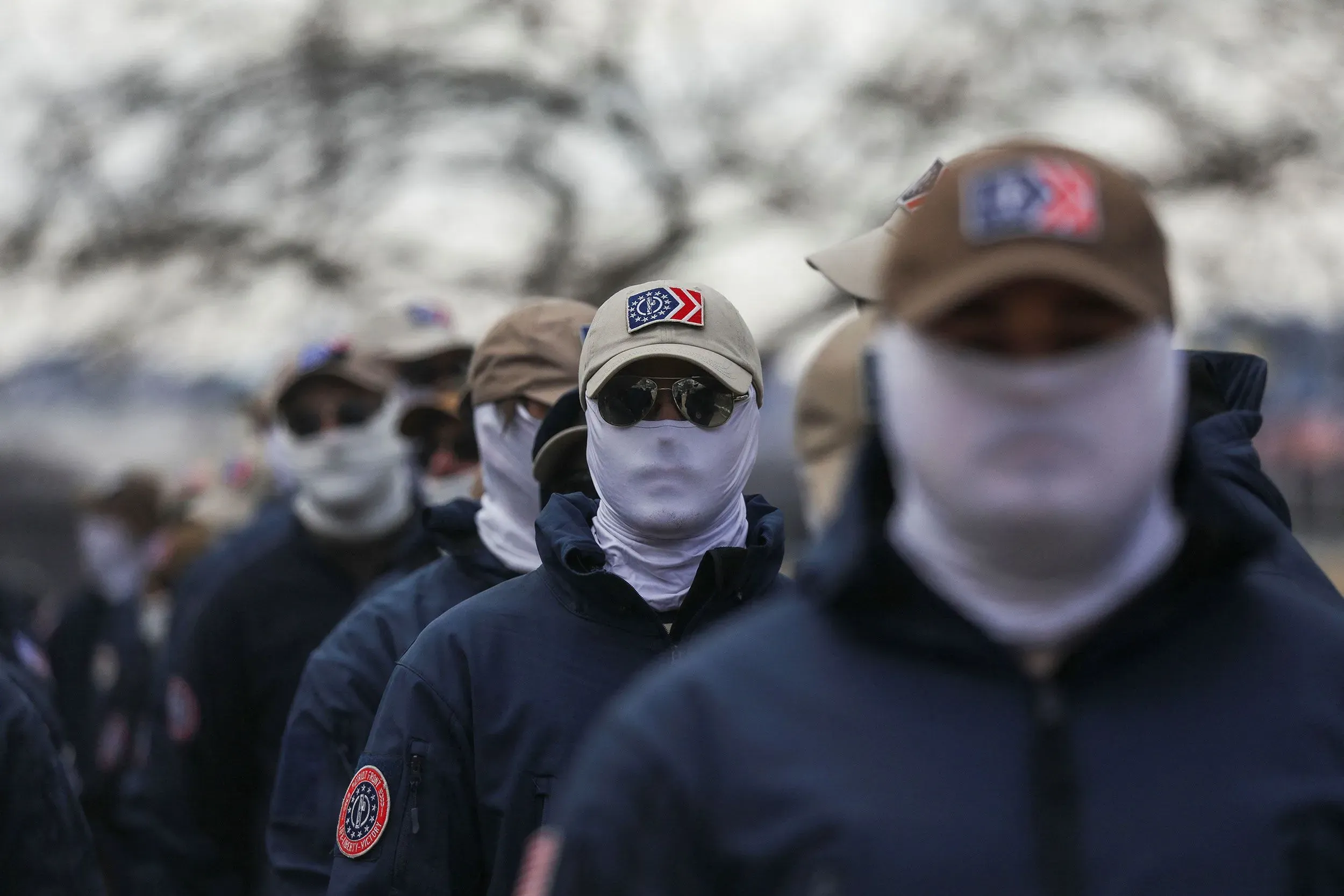 مجموعة من الأفراد يرتدون ملابس موحدة وقبعات، مع تغطية وجوههم بأقنعة بيضاء، أثناء تجمع في ولاية تينيسي.