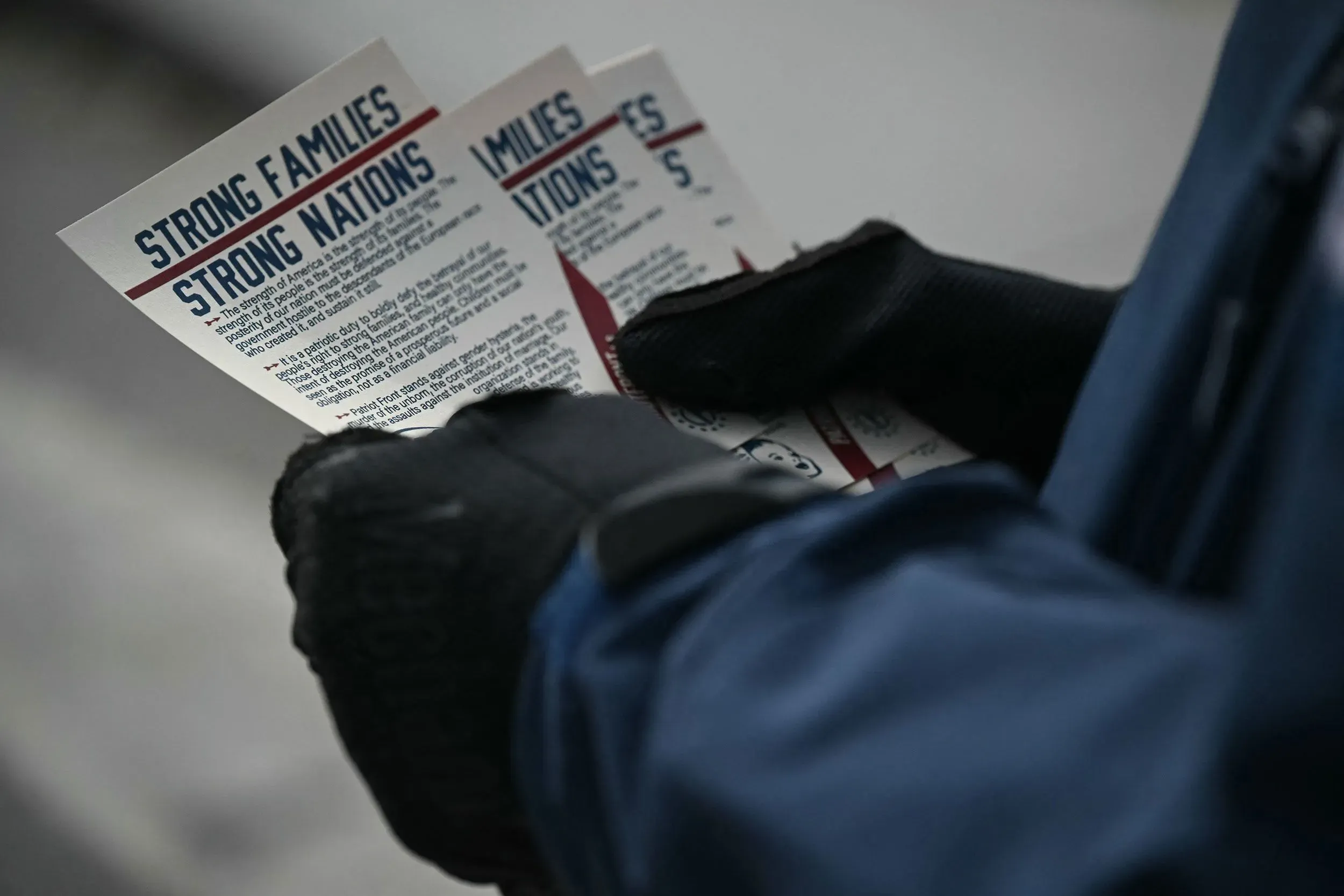 تظهر اليدين المرتديتين للقفازات holding عدة منشورات تتحدث عن "عائلات قوية وأمم قوية"، مما يعكس نشاطات جماعة جبهة باتريوت في تينيسي.