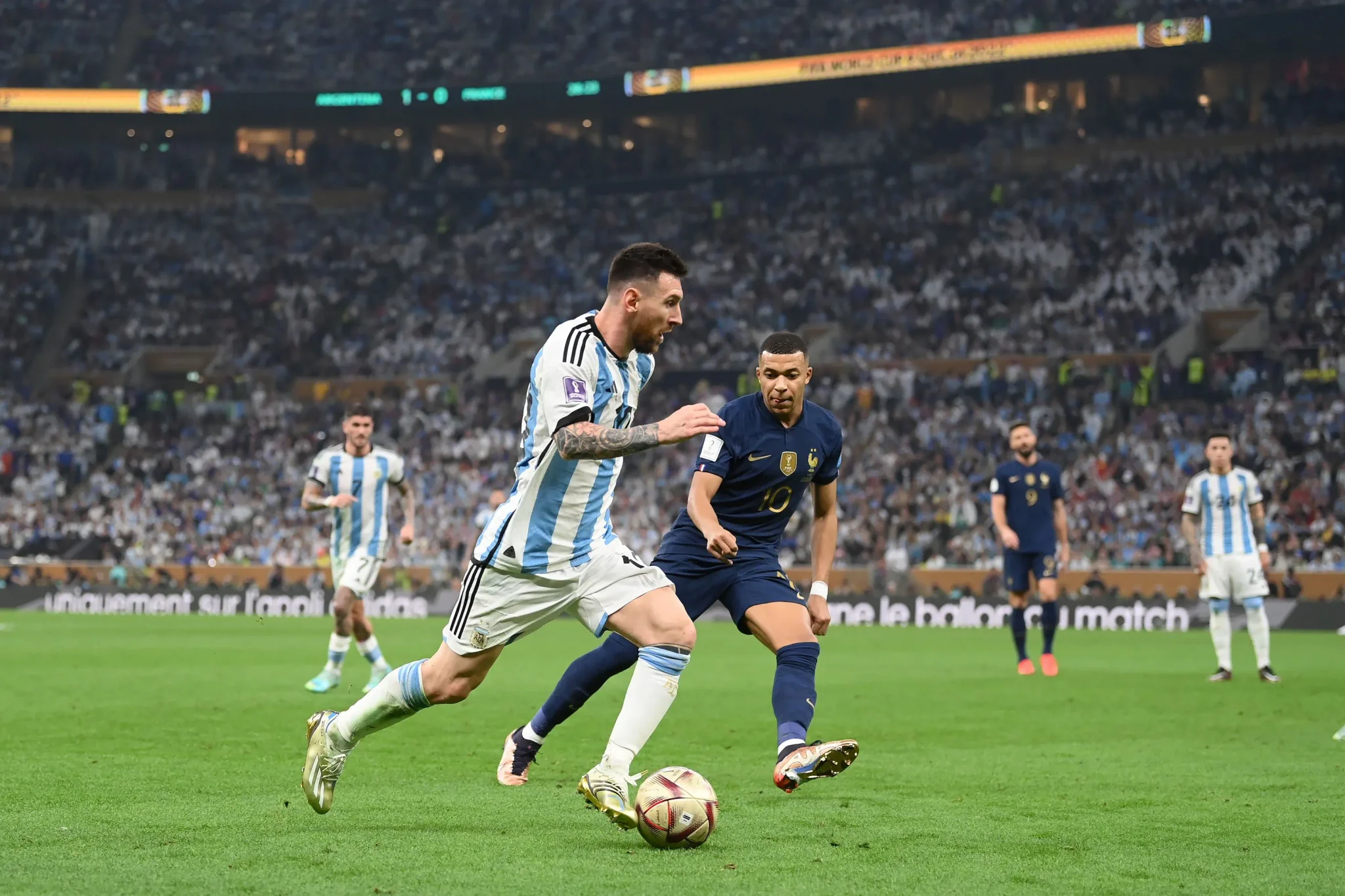 كيليان مبابي في مواجهة مع ليونيل ميسي خلال مباراة فرنسا والأرجنتين في كأس العالم، مع جمهور متحمس في الخلفية.