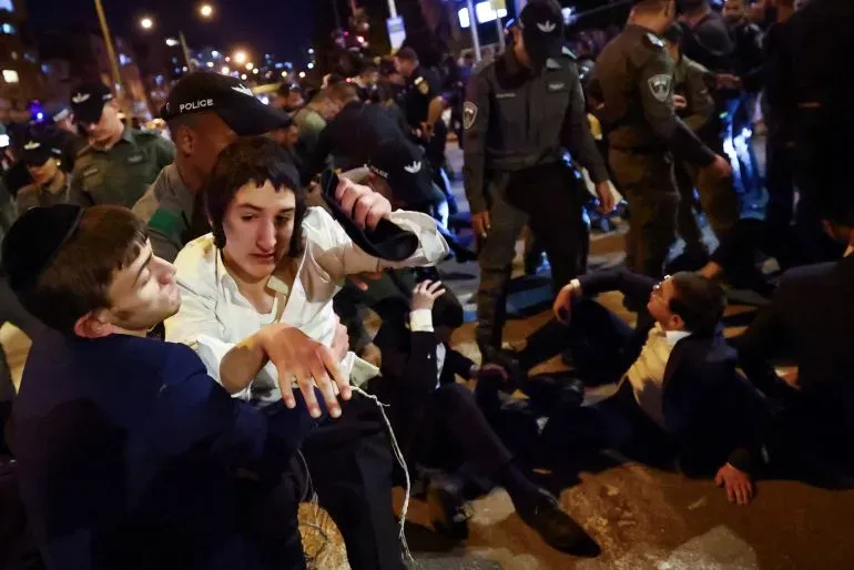 احتجاجات في تل أبيب ضد حرب غزة، تظهر متظاهرين يرتدون ملابس دينية، بينما يتدخل رجال الشرطة.