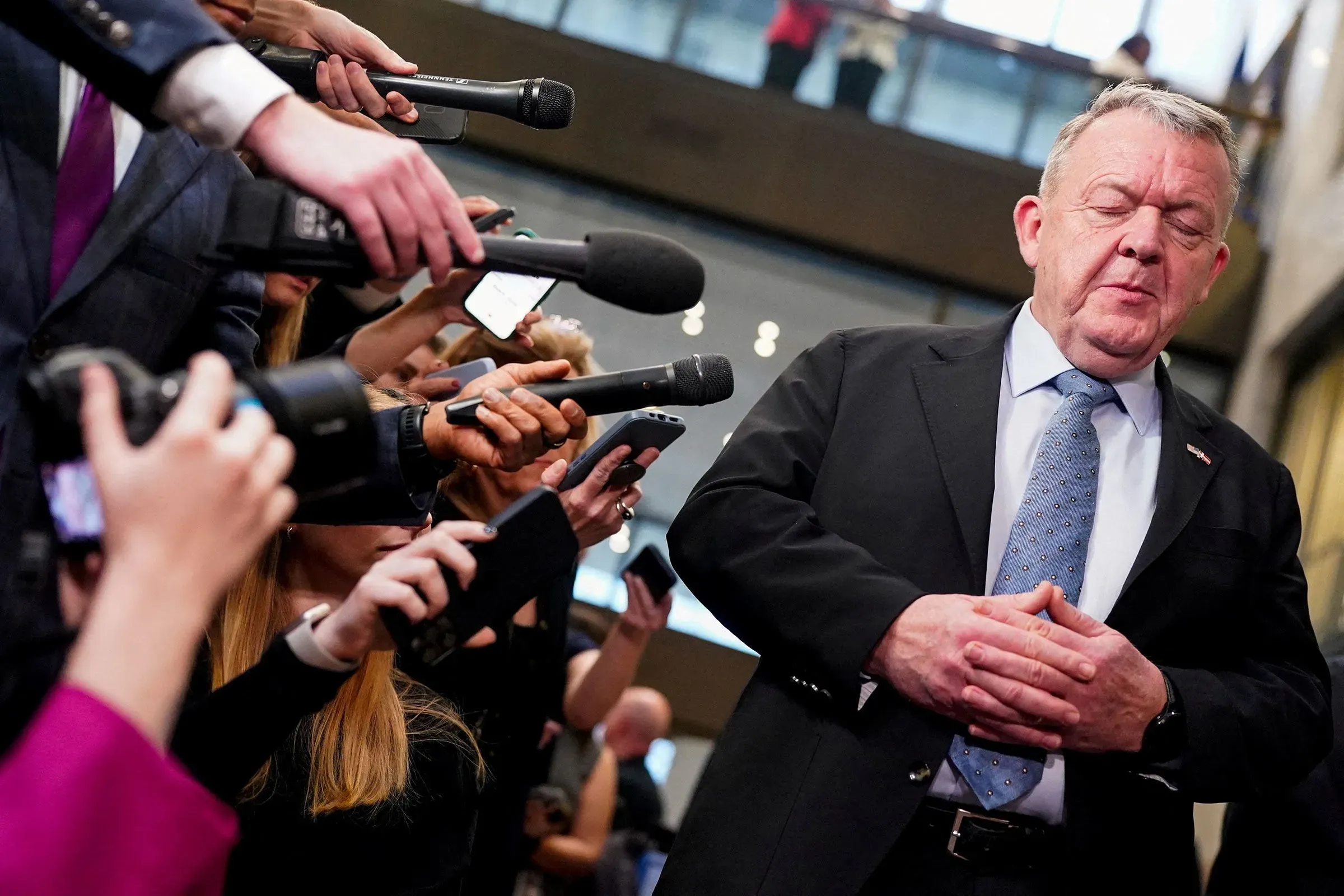 رجل يقف أمام مجموعة من الصحفيين الذين يحملون ميكروفونات، مع تعبير جدي، في مؤتمر صحفي حول تصريحات ترامب عن غرينلاند.