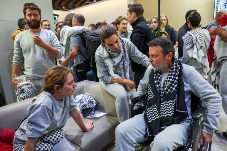 ناشطون أجانب في مطار إسطنبول بعد ترحيلهم من إسرائيل، يرتدون الأوشحة الفلسطينية، يتبادلون الحديث في أجواء من التعاطف.
