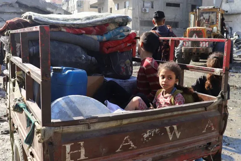 عائلة فلسطينية في شاحنة صغيرة محملة بالأمتعة والبطانيات، وسط دمار مدينة غزة، في ظل النزوح بسبب الهجمات الإسرائيلية.