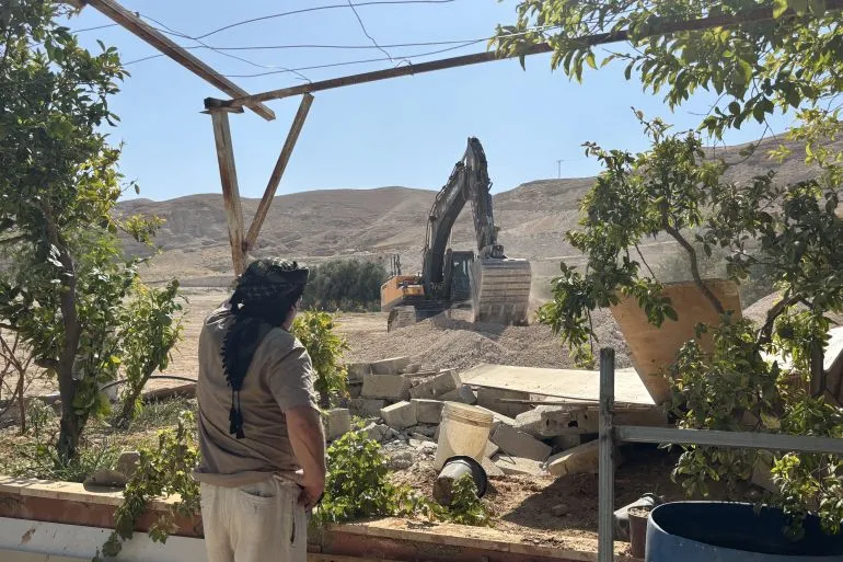 رجل فلسطيني يراقب جرافة إسرائيلية تهدم منازل في حي عين الديوك بأريحا وسط تدمير واسع للممتلكات الفلسطينية.