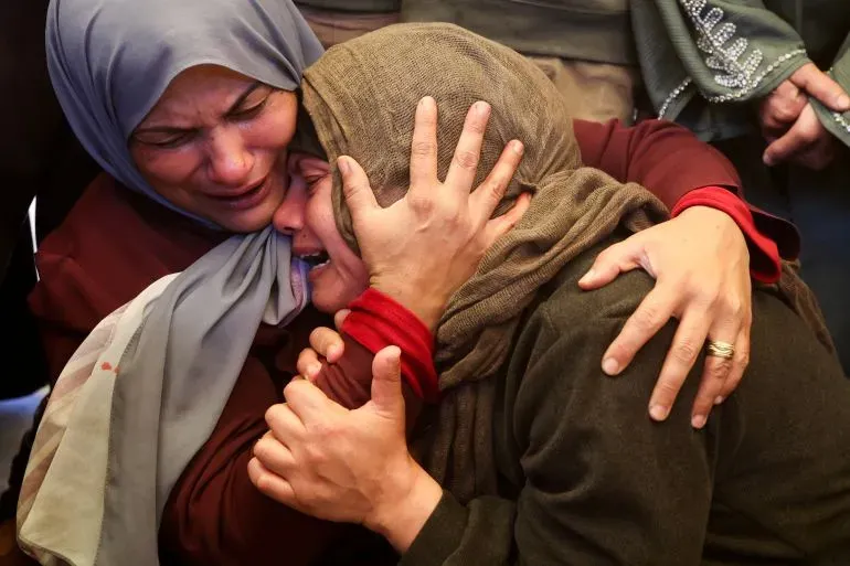 امرأتان فلسطينيتان تعبران عن حزن عميق أثناء العزاء، حيث تحتضنان بعضهما في مشهد مؤثر يعكس الألم الناتج عن الأحداث الأخيرة في غزة والضفة الغربية.